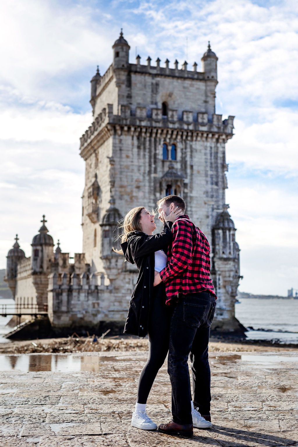 Couple kissing in front of the historic Belem Tower in Lisbon, Portugal on a sunny day.