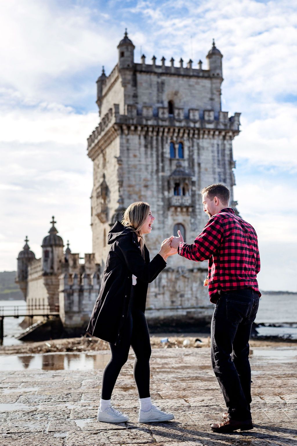 Couple sharing a romantic moment in front of the historic Belem Tower in Lisbon, Portugal on a cloudy day.