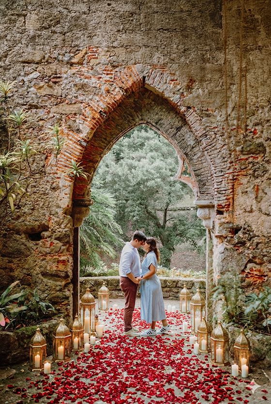 A romantic archway decorated with red rose petals and lanterns creates a dreamy atmosphere for a special moment.