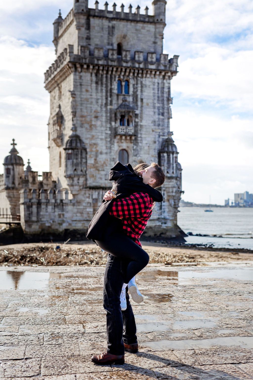 Couple embracing romantically in front of the historic Torre de Belem tower in Lisbon, Portugal.