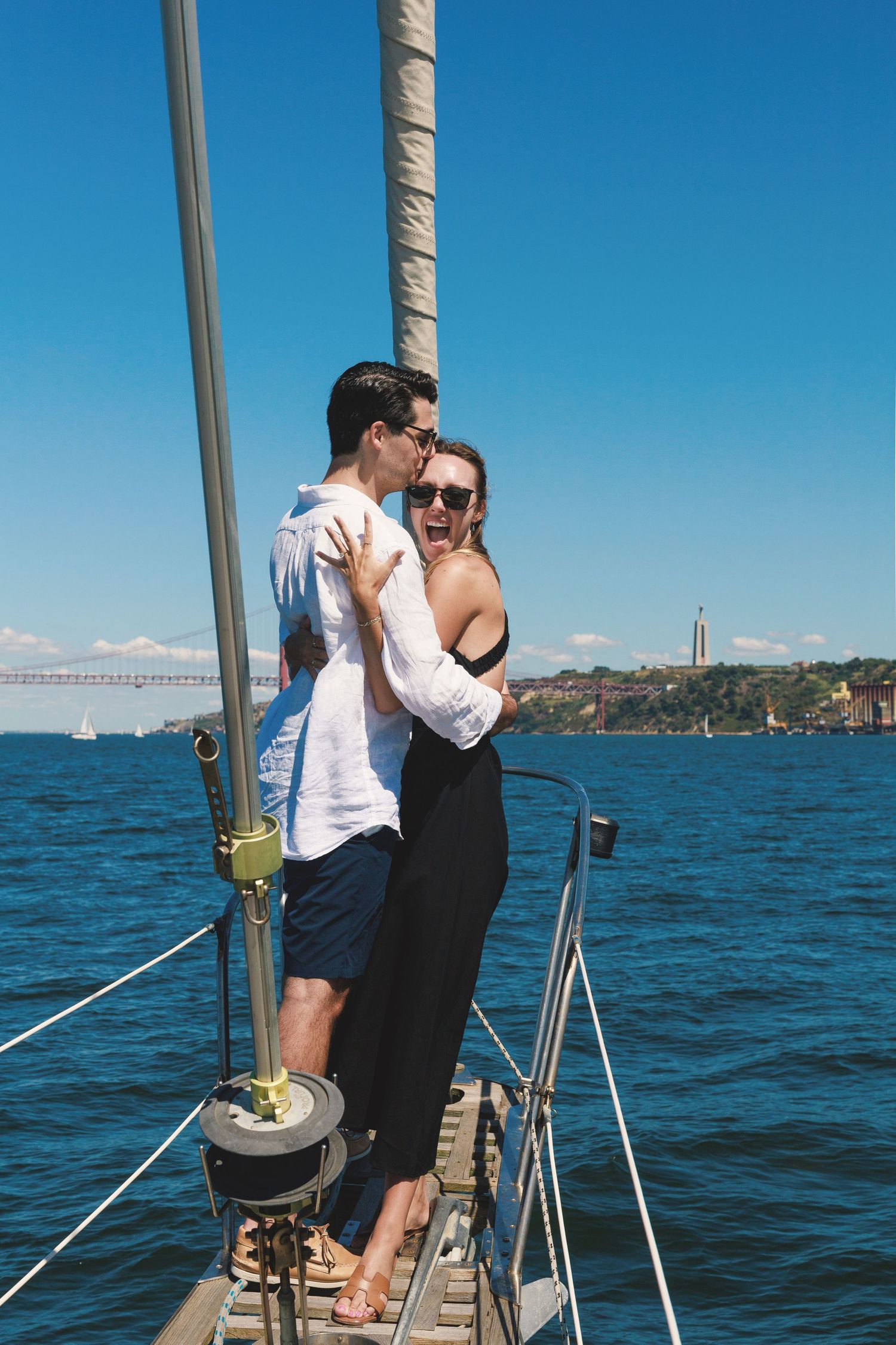 A couple shares a romantic moment while sailing on a boat with the San Francisco Bay and bridge visible in the background.