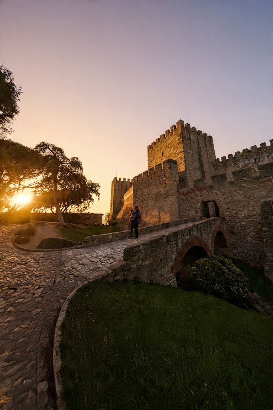 Ancient stone castle walls and towers at sunset with dramatic lighting illuminating the medieval fortress architecture.