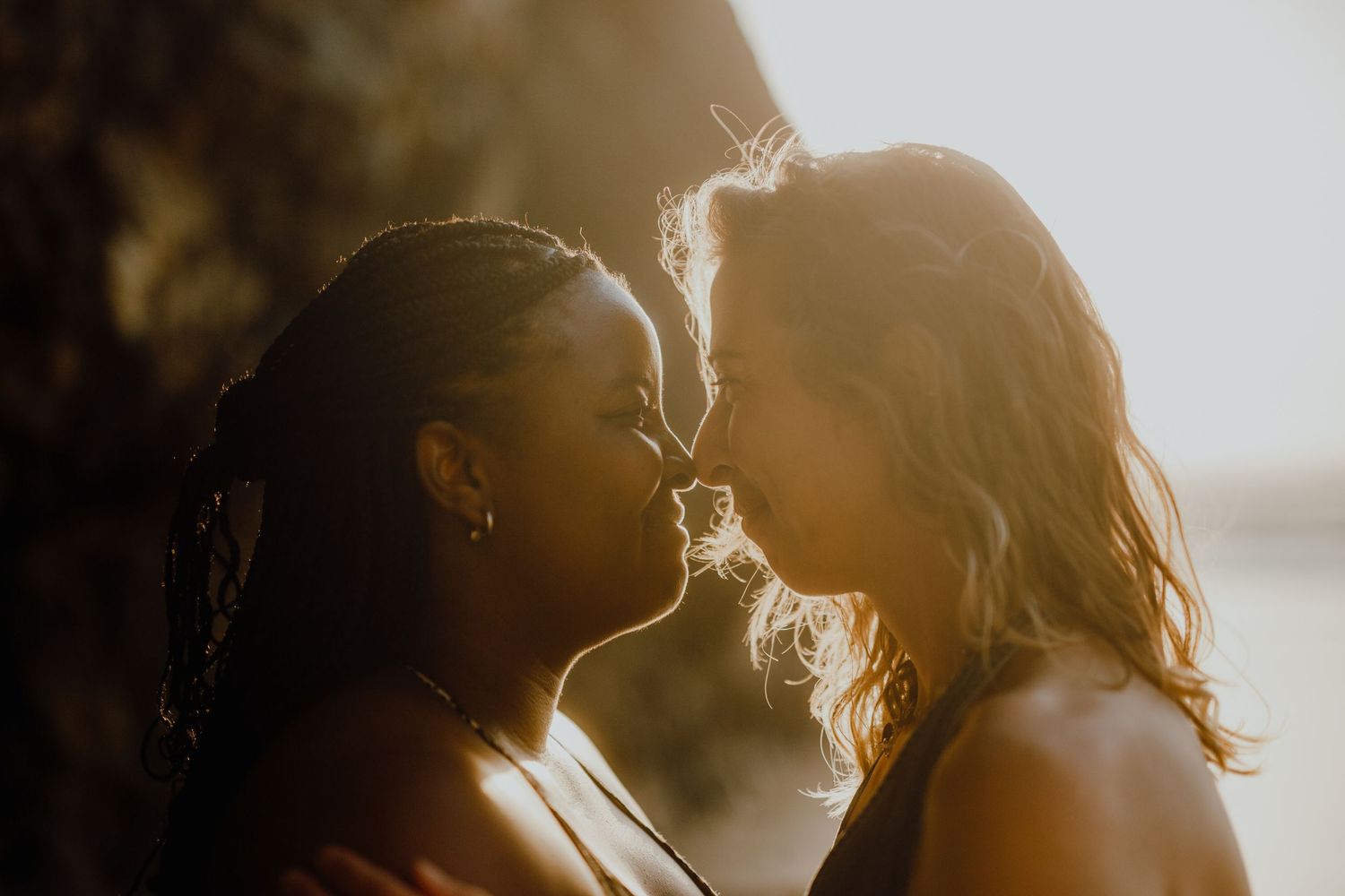 A romantic couple sharing an intimate moment in golden sunlight with their faces close together.