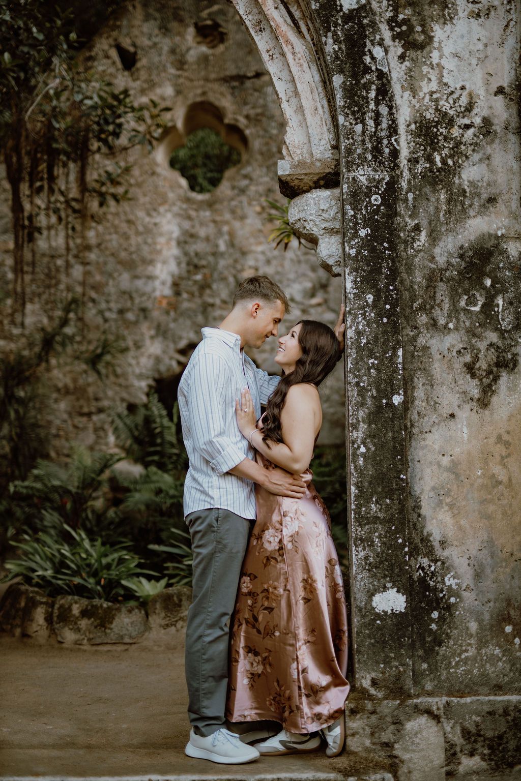 A romantic couple shares tender moments against weathered stone pillars in an outdoor setting.