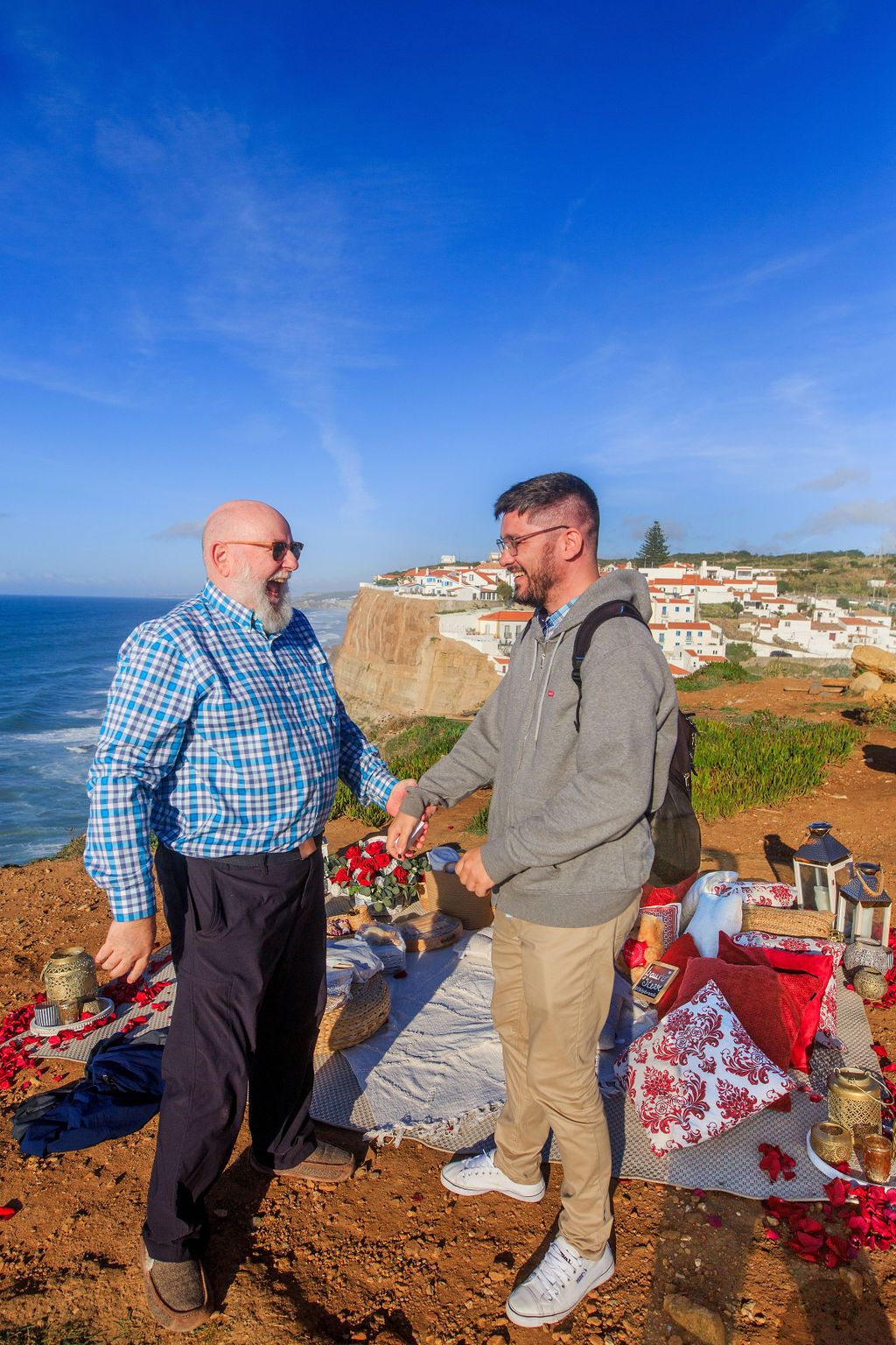 Two men shaking hands at a scenic coastal picnic spot with ocean views and a white village in Portugal.