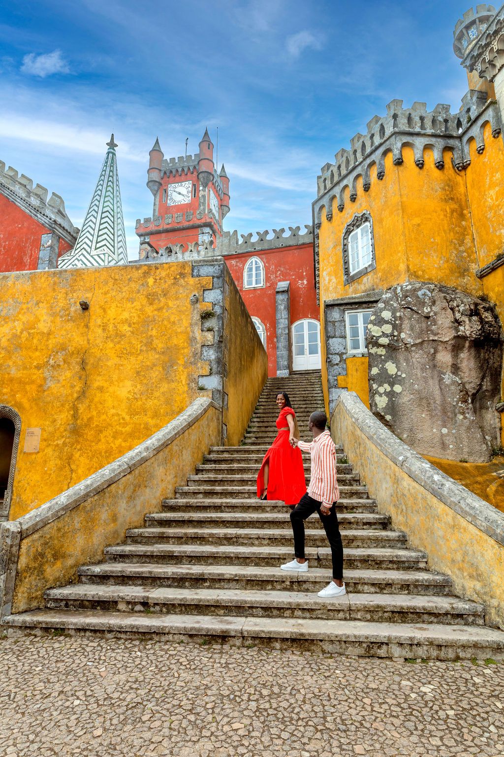 Colorful architectural details of Pena Palace in Sintra, Portugal showing yellow walls and stone steps against blue sky.