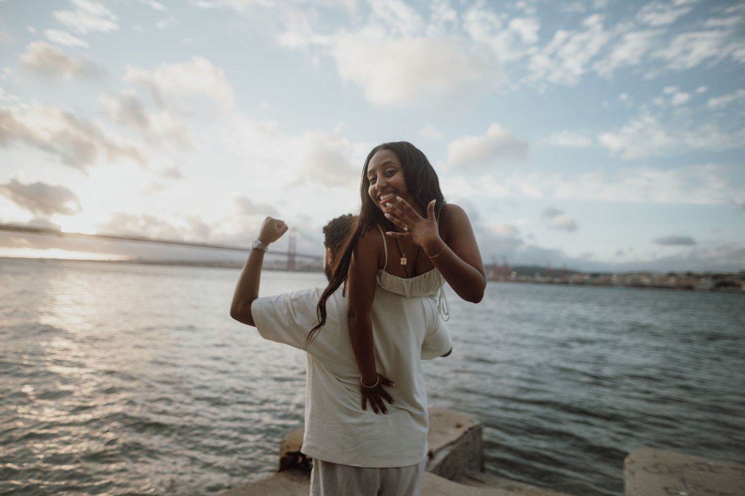 A person in a white dress dances joyfully along the beach at sunset with ocean waves in the background.