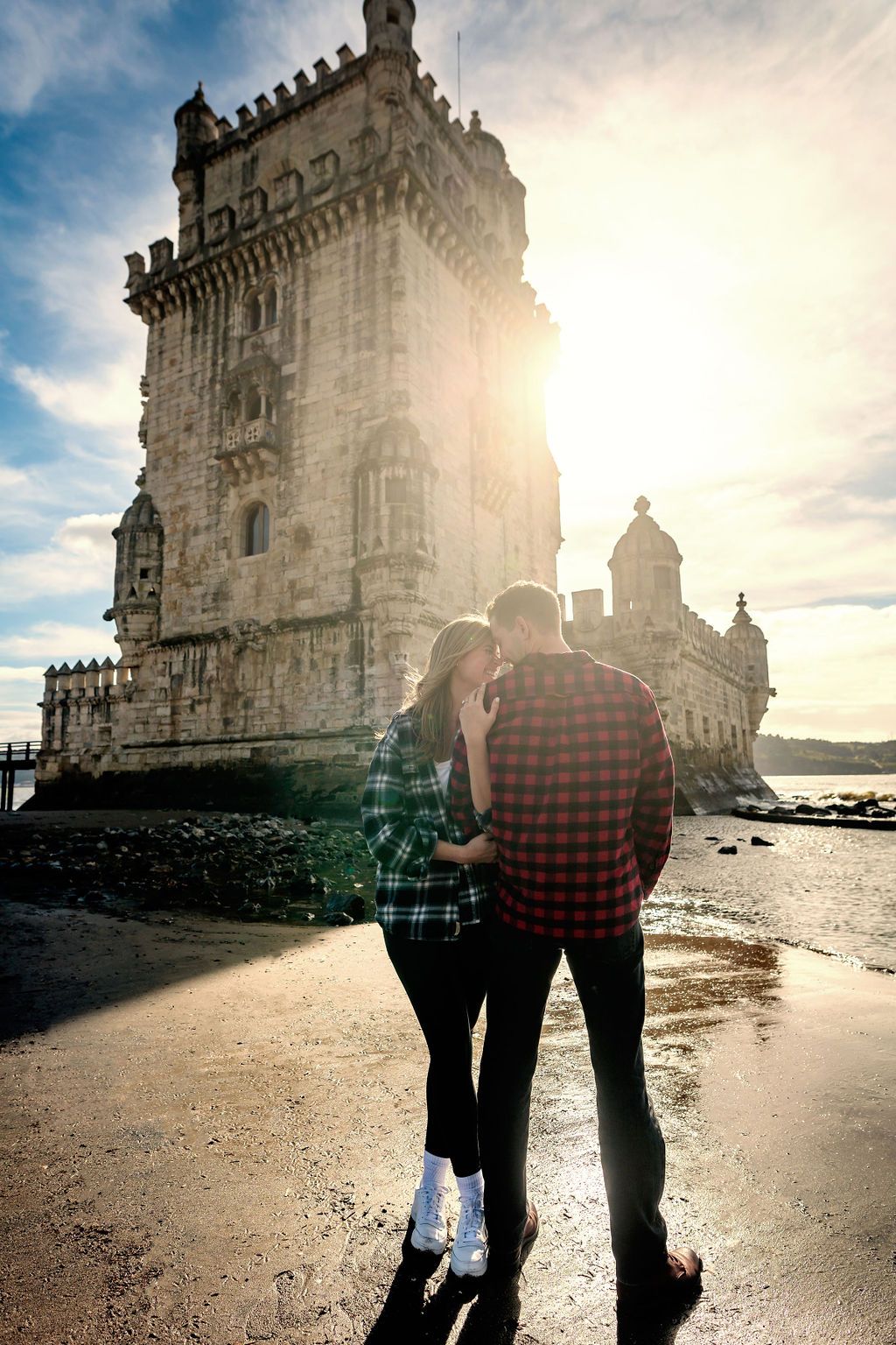 Couple embracing romantically in front of the historic Torre de Belem tower in Lisbon, Portugal at sunset.