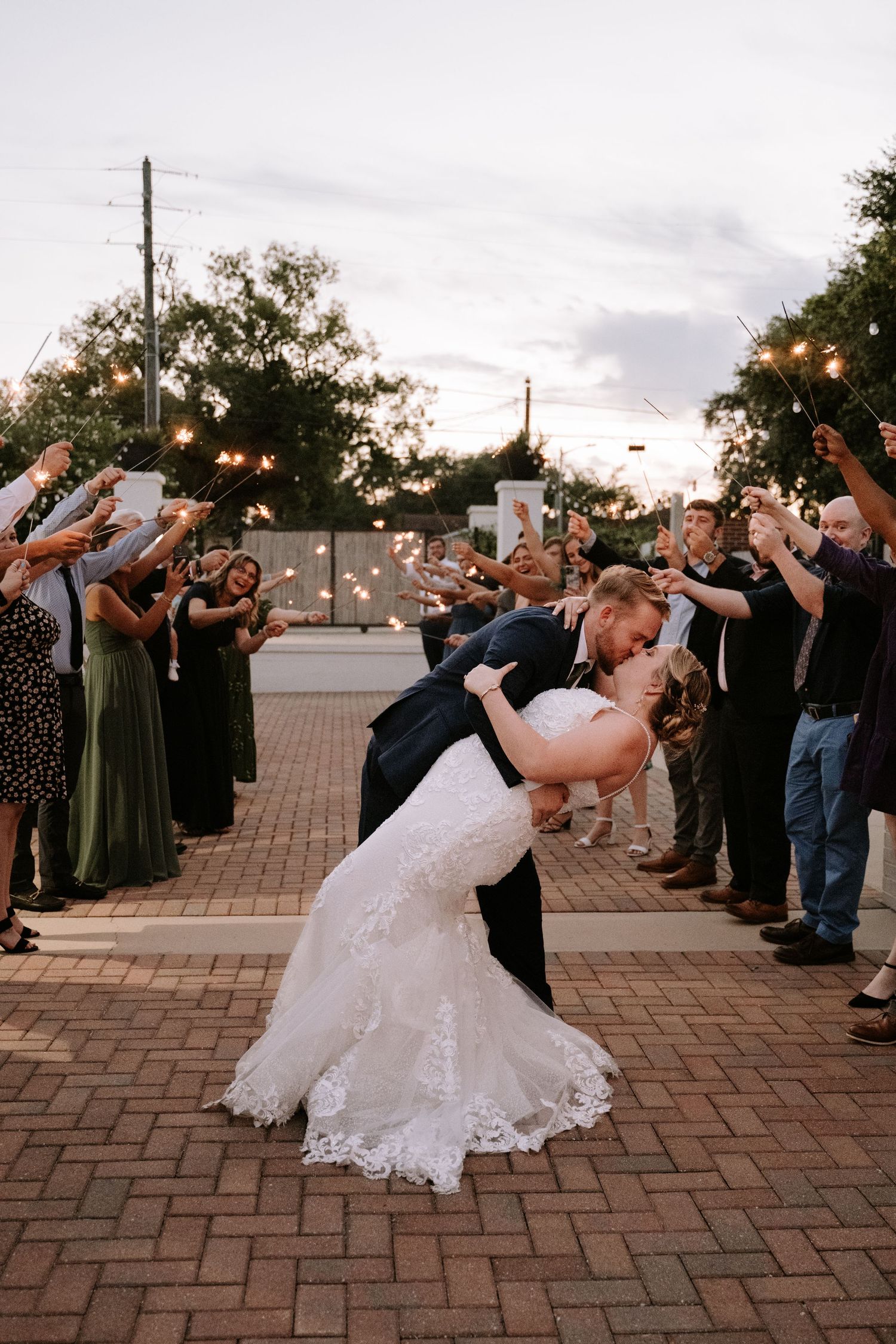 A romantic dip sequence at a wedding reception shows the couple performing a dramatic dance move on brick pavers at dusk.