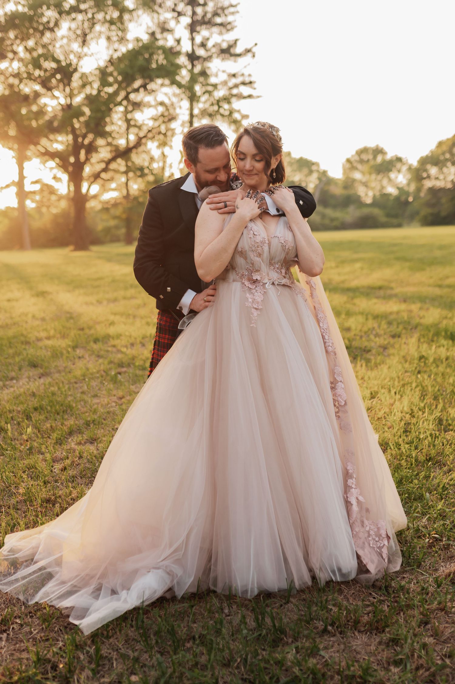 Bride and groom embrace at golden hour sunset, bride wearing blush floral ball gown wedding dress outdoors.
