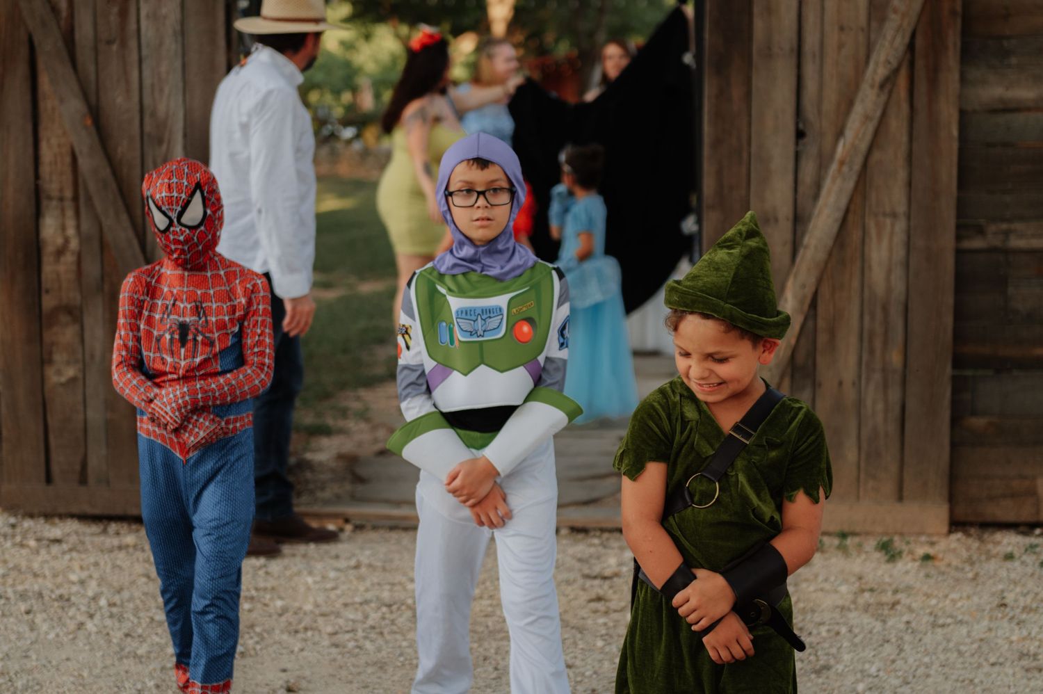 Children in Halloween costumes including Spider-Man, Buzz Lightyear, and Peter Pan pose outdoors near a rustic barn.