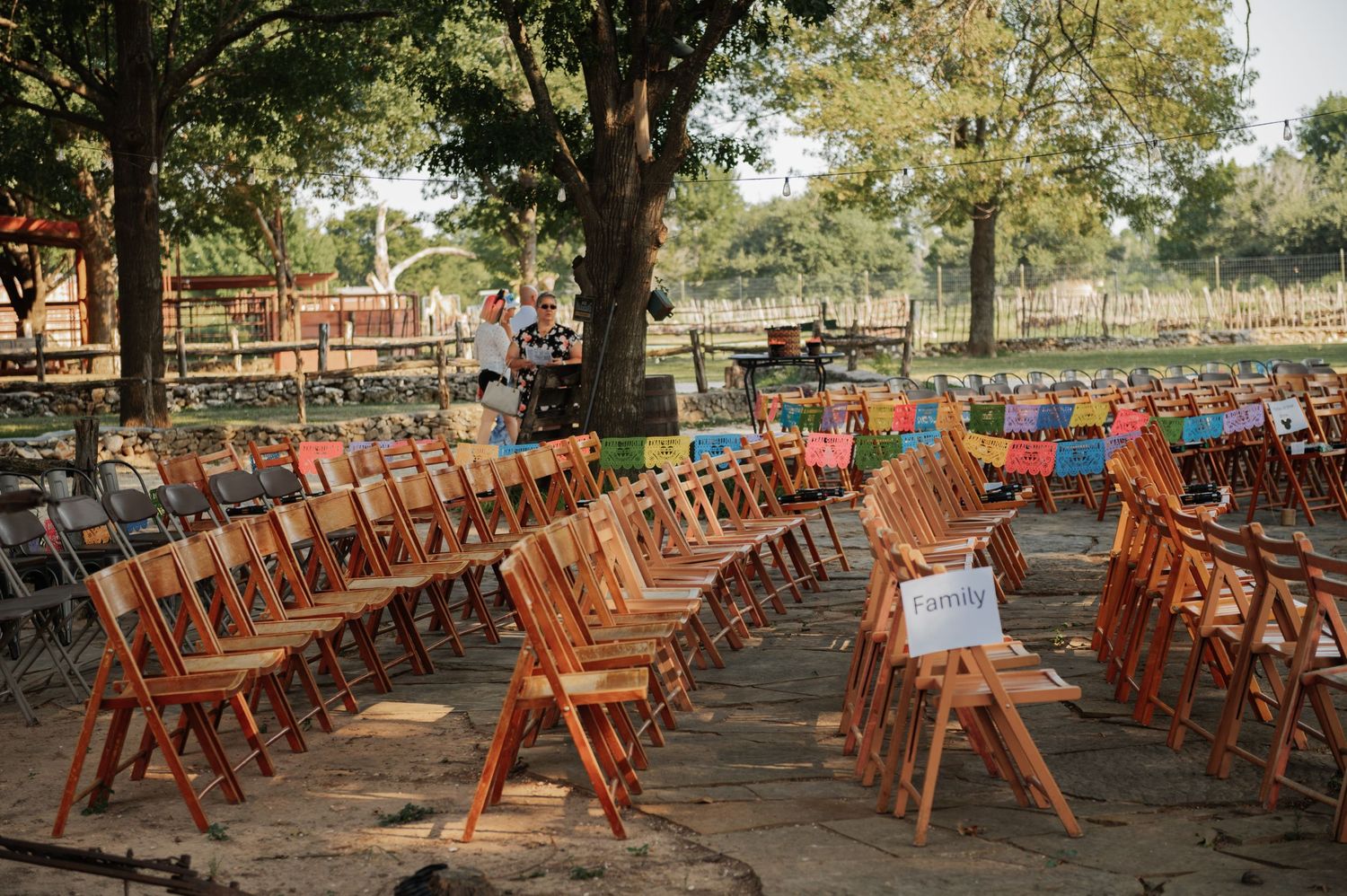 Rows of wooden folding chairs arranged outdoors under trees for a rustic wedding ceremony.