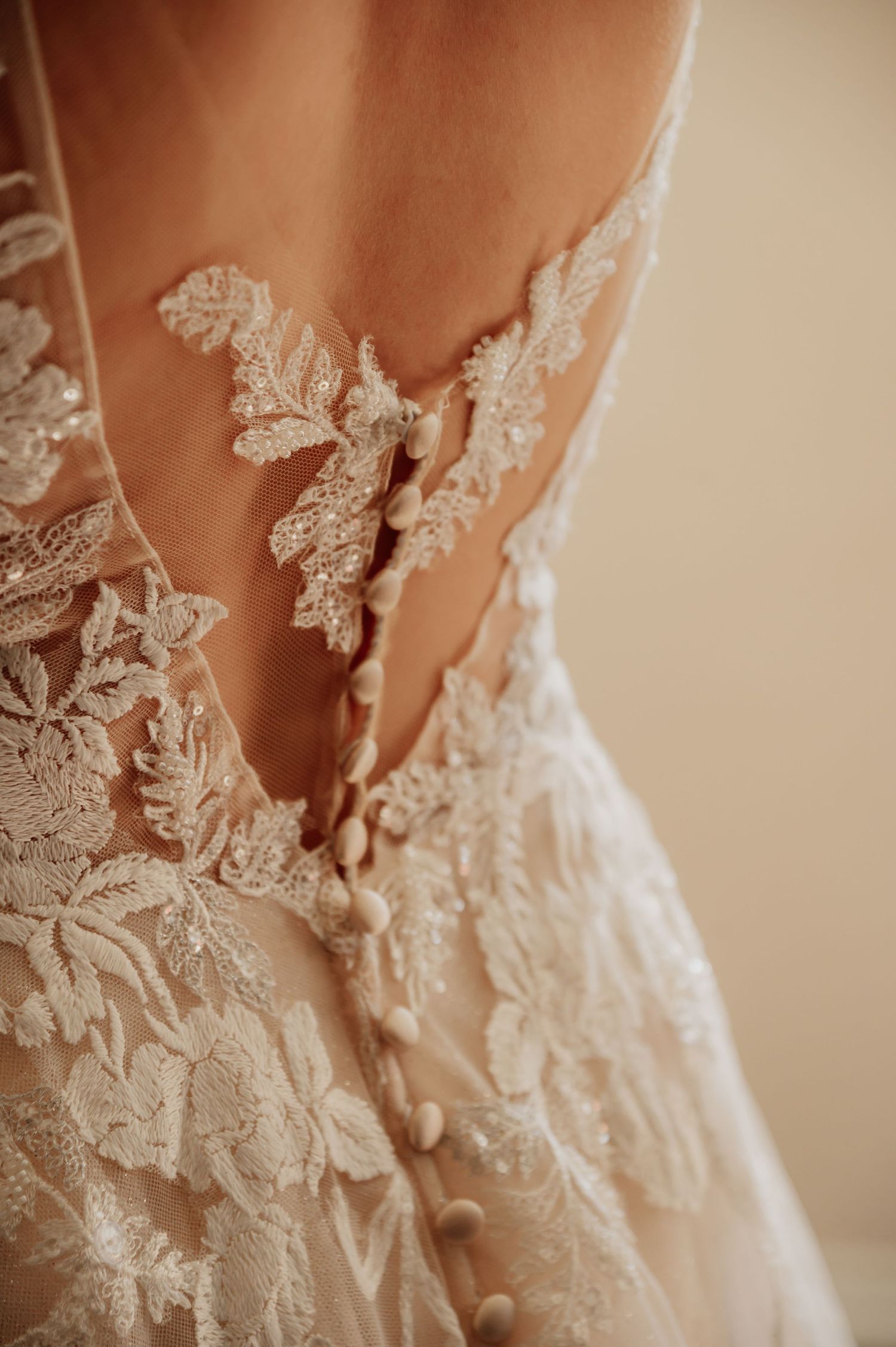 Close-up of intricate lace applique detailing on the back of an elegant white wedding gown with sheer fabric.
