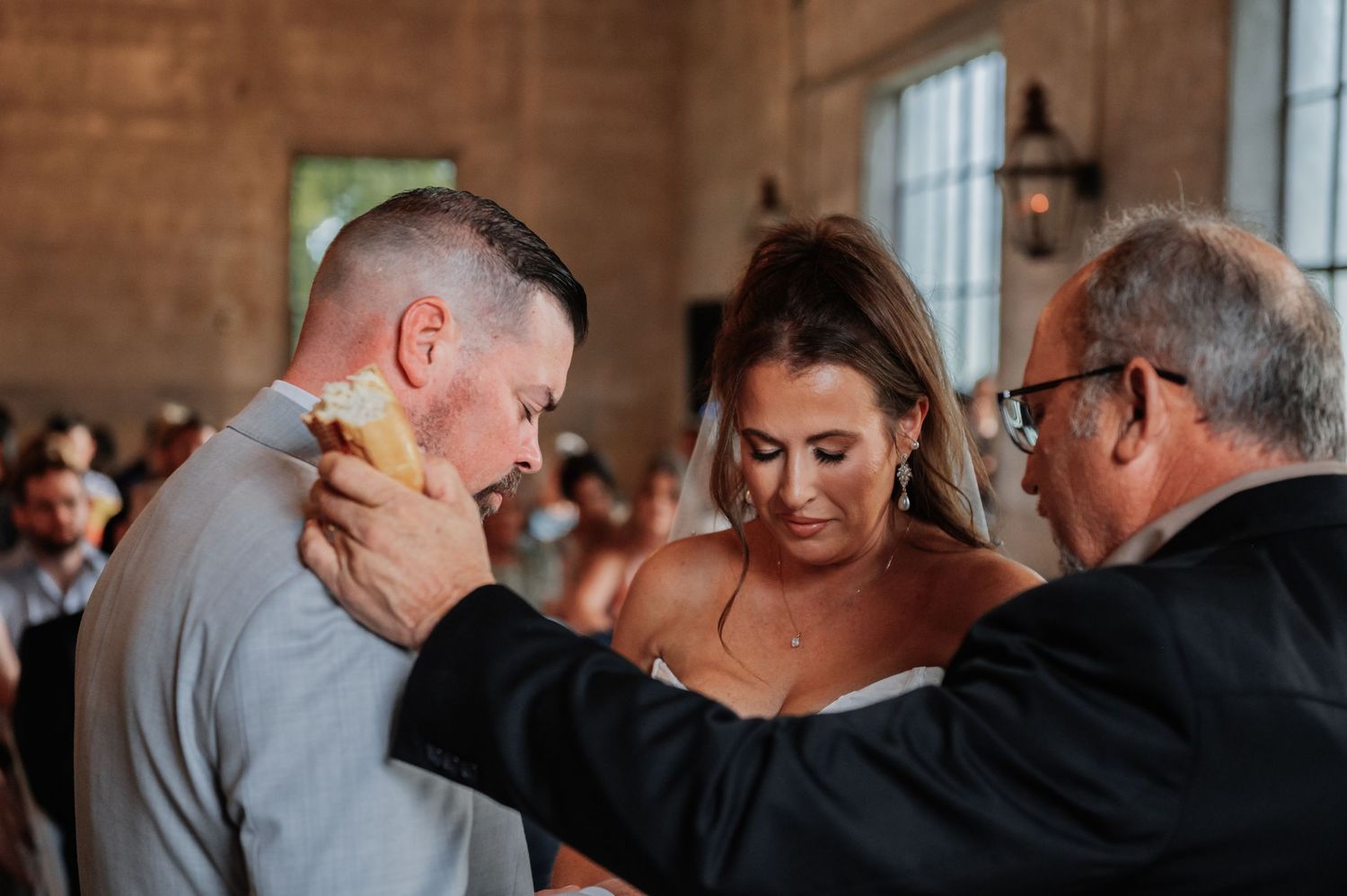 Emotional wedding moment as groom wipes tears during heartfelt ceremony blessing with officiant.