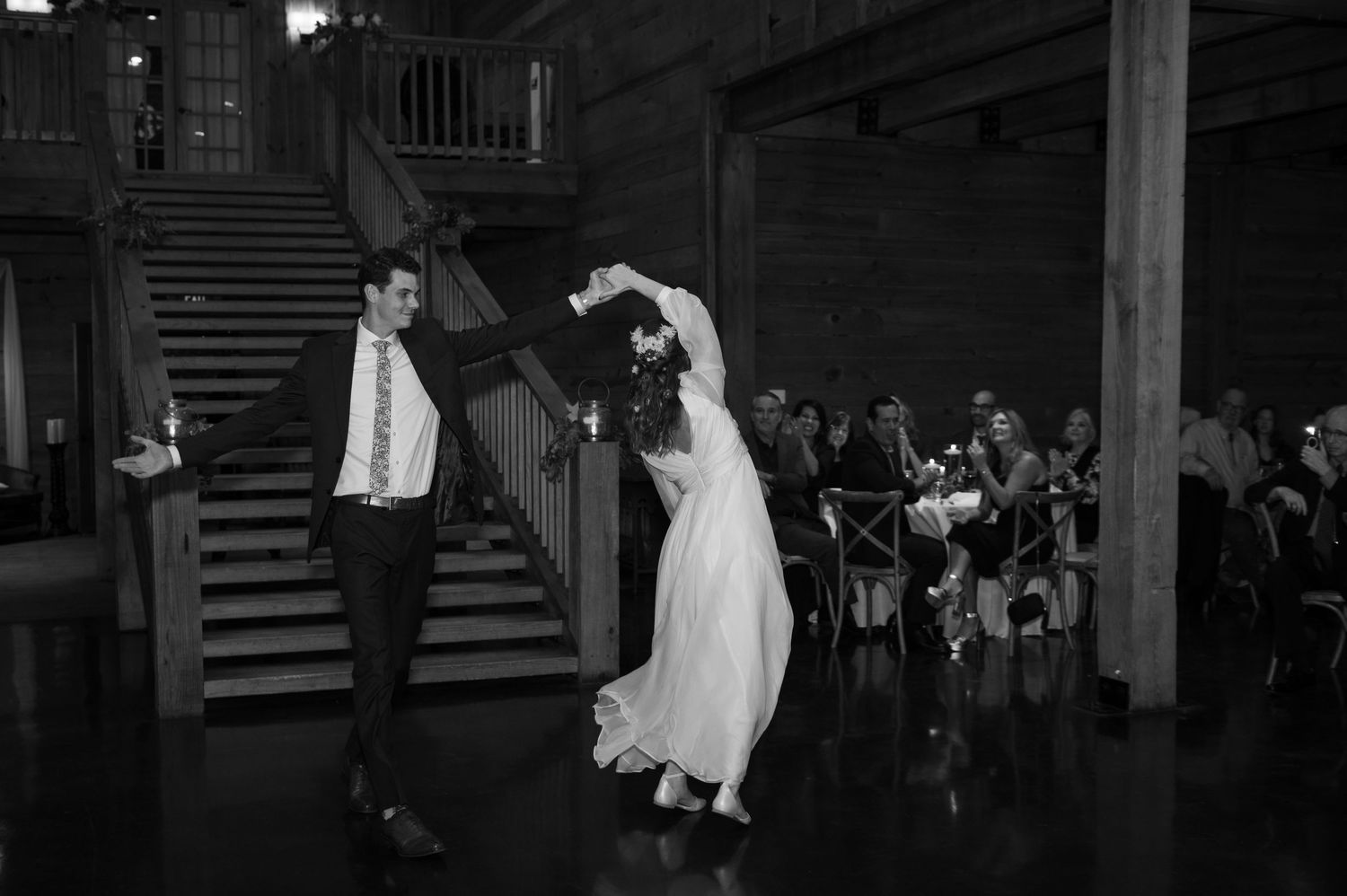 Black and white photo of bride and groom sharing first dance at wedding reception near grand staircase.