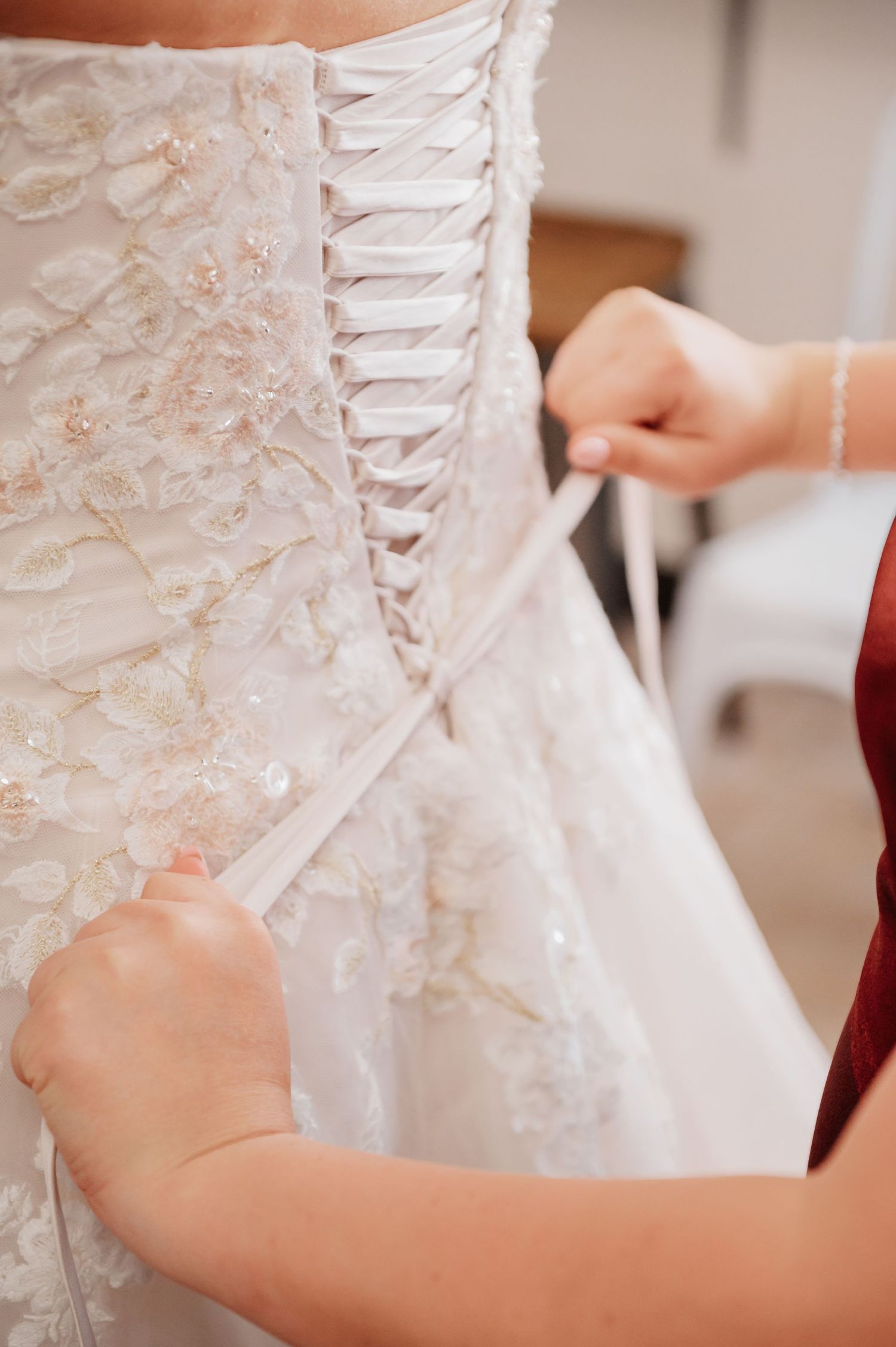 Hands lacing up the back of a white beaded corset wedding dress with ribbon ties.