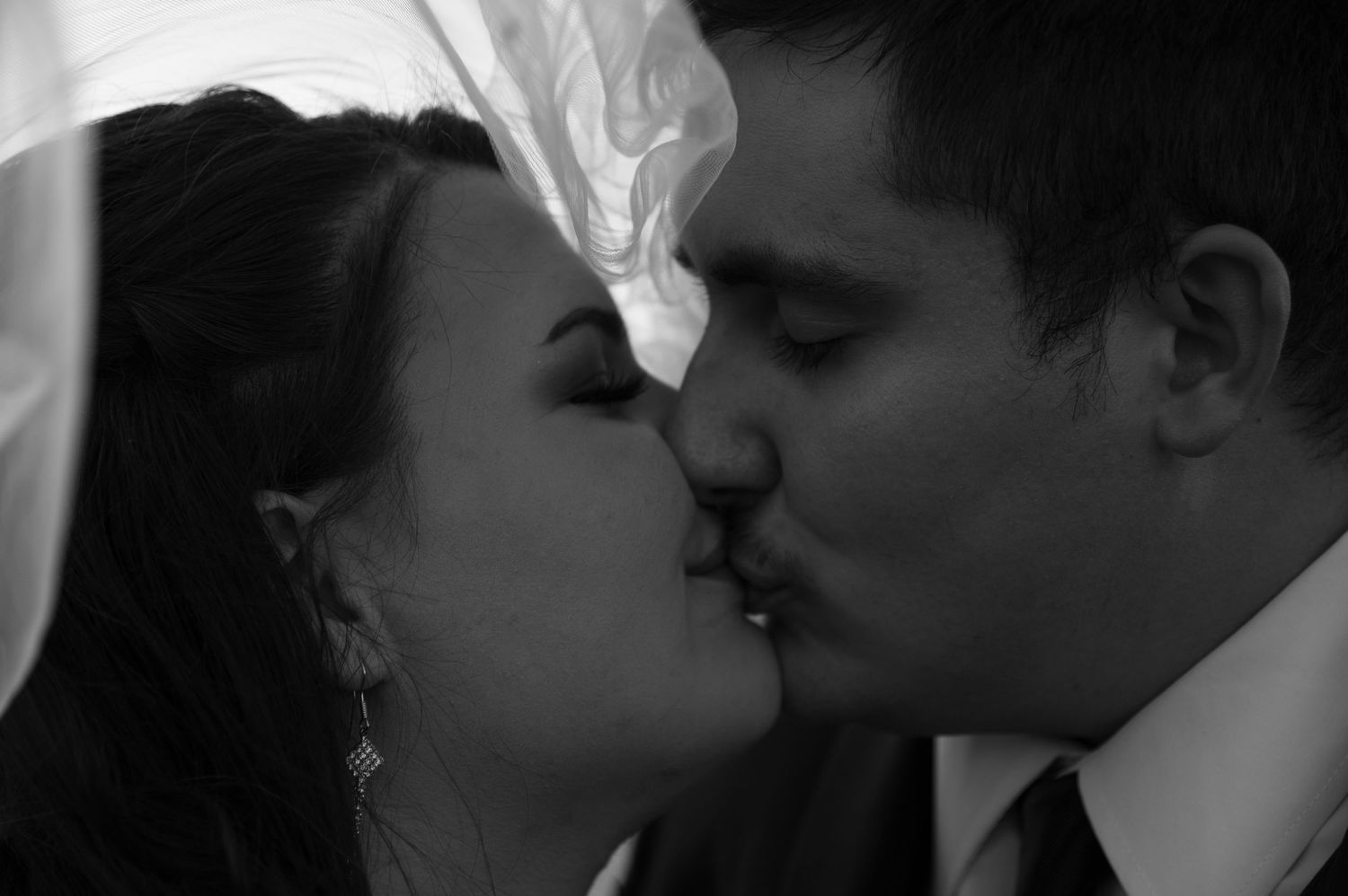 Black and white photo of a bride and groom sharing a romantic kiss on their wedding day.