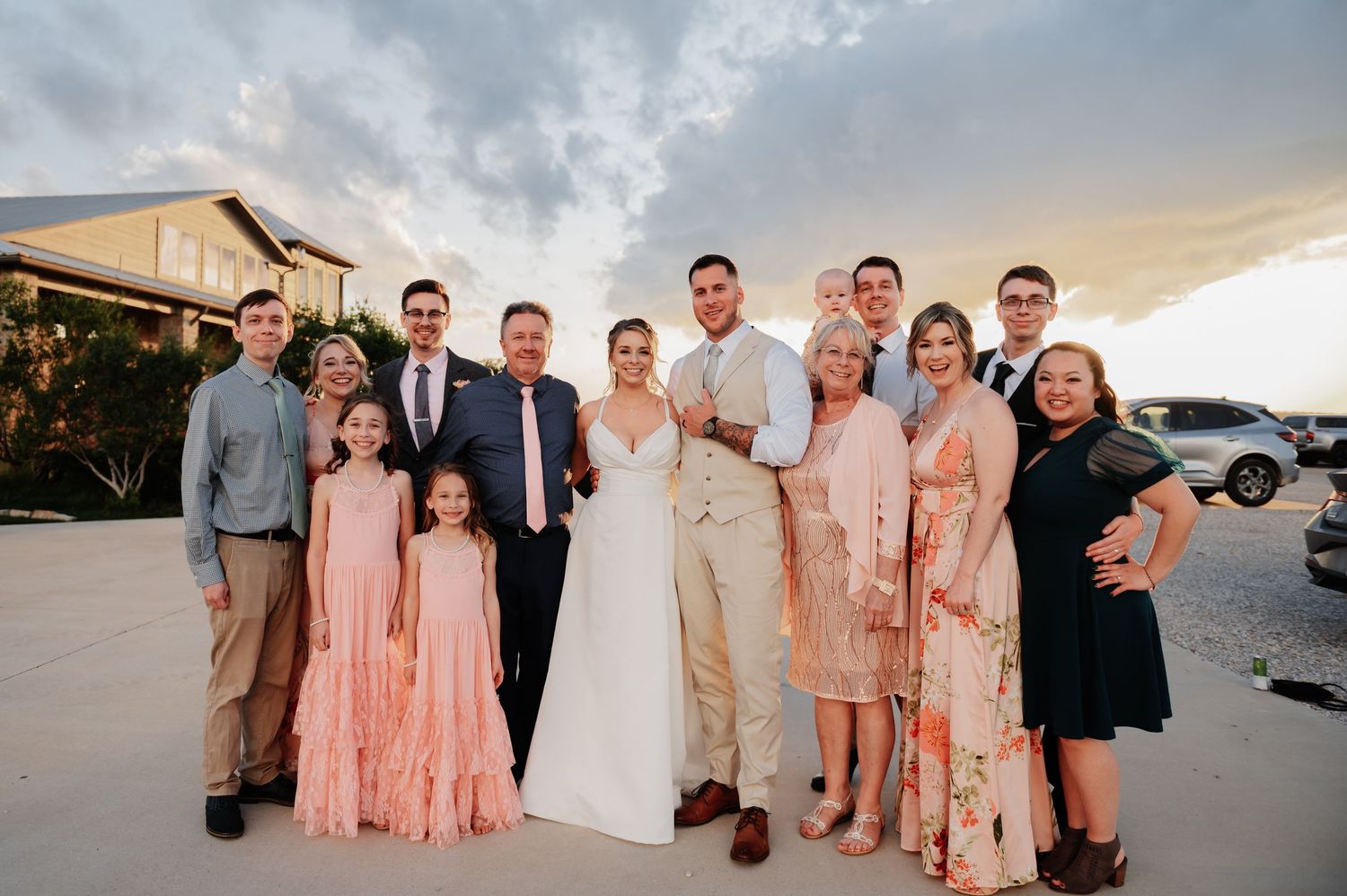 Family group photo at an outdoor wedding celebration, with bride and groom surrounded by relatives at sunset.