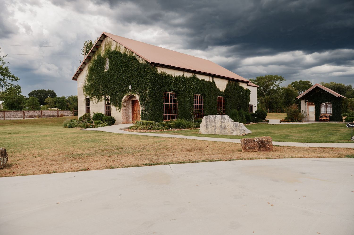 Ivy-covered rustic wedding venue with stone walls and red accents under dramatic stormy skies.