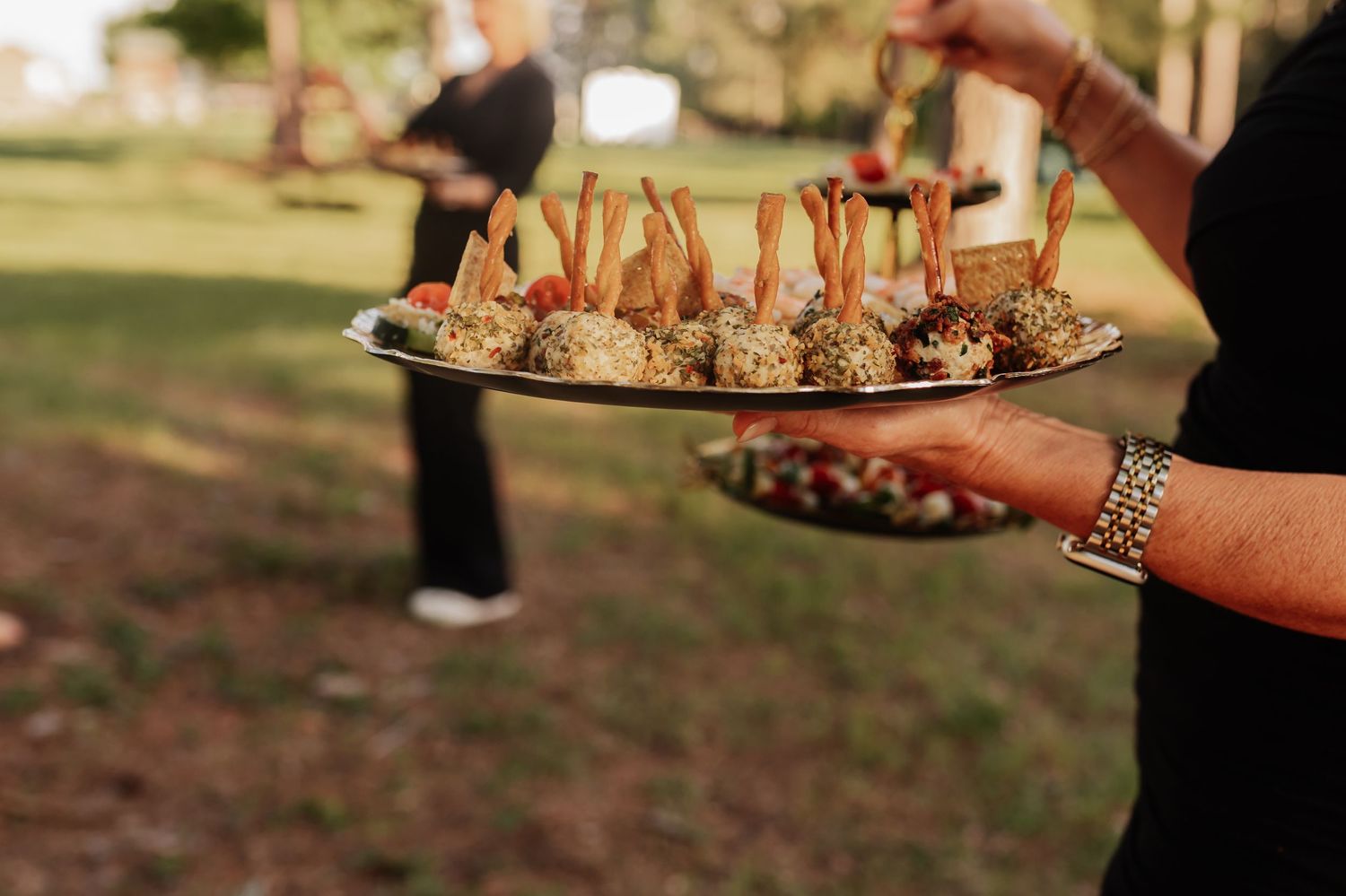 Catering staff serving elegant appetizers on silver trays at an outdoor event.