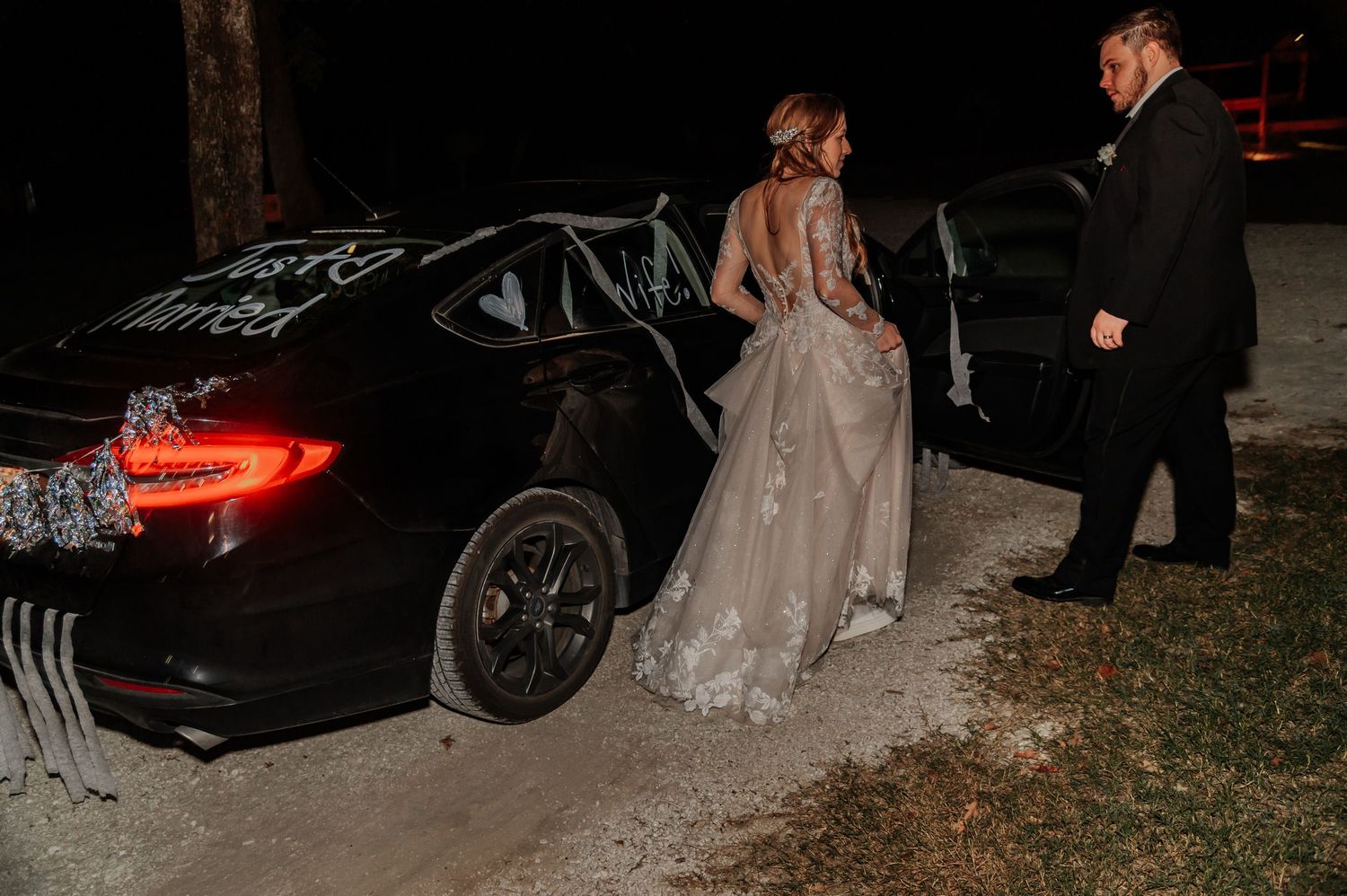 Bride and groom beside Just Married car at night outdoor wedding celebration.