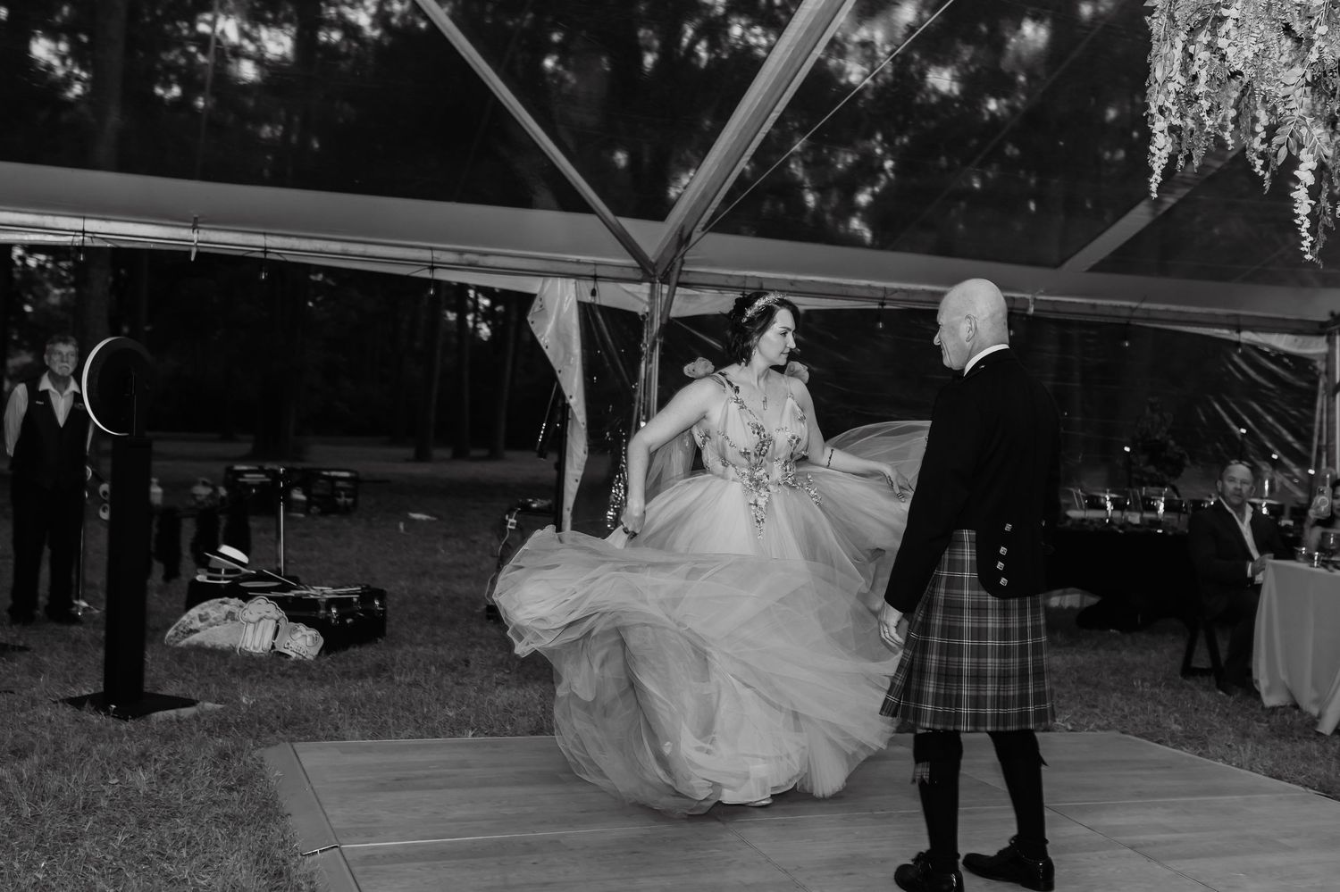 Bride twirling in elegant gown during first dance with groom in kilt under outdoor tent at wedding reception.