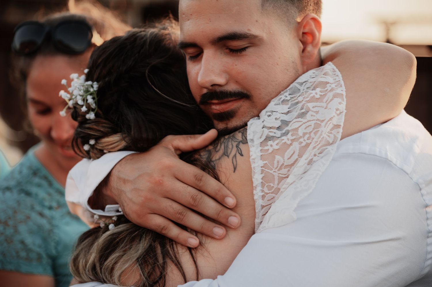 Groom with tattoos and mustache embracing bride with floral hair accessories at wedding celebration.