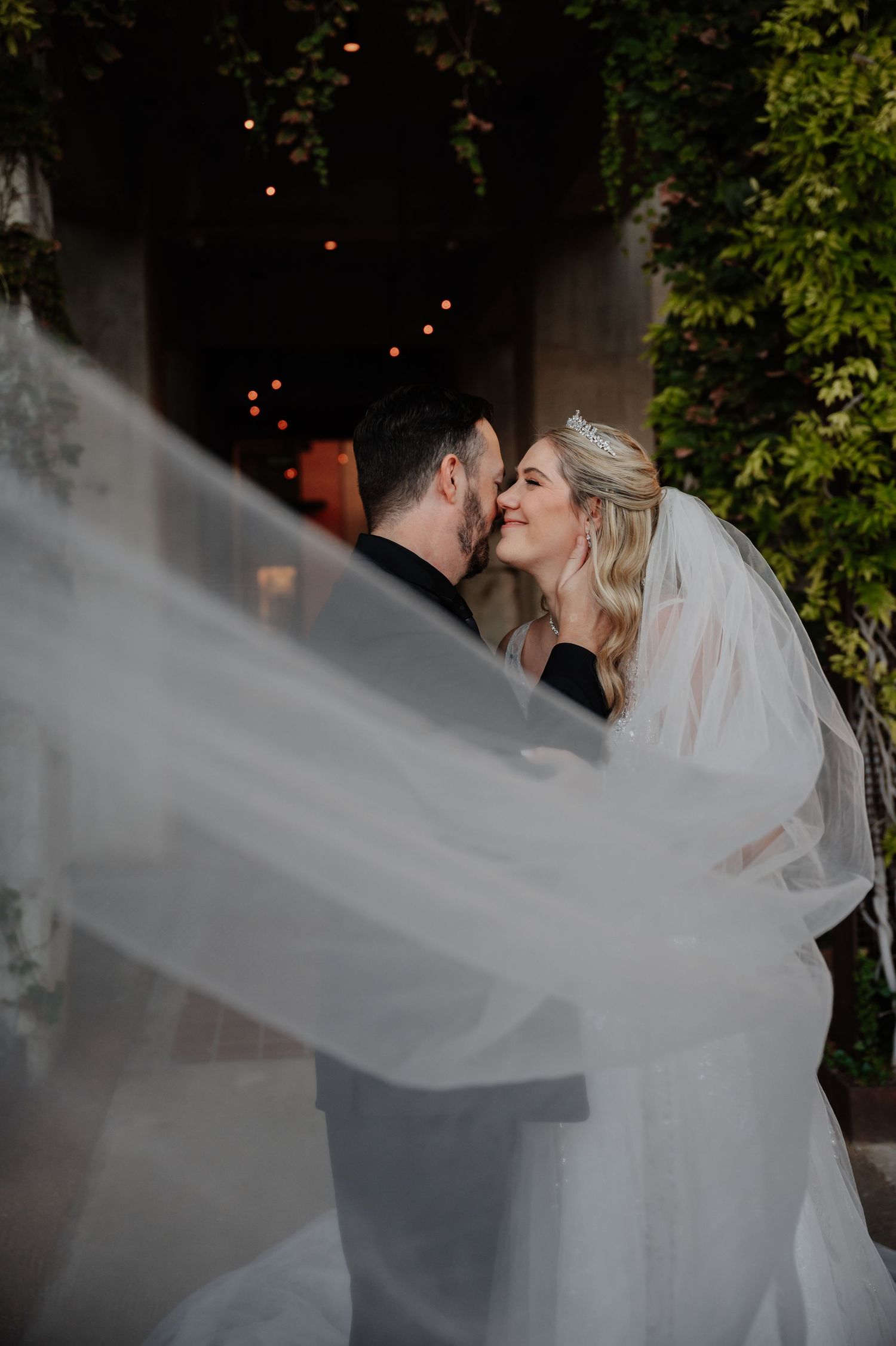 Romantic wedding photo of bride and groom kissing as flowing veil billows in the foreground.
