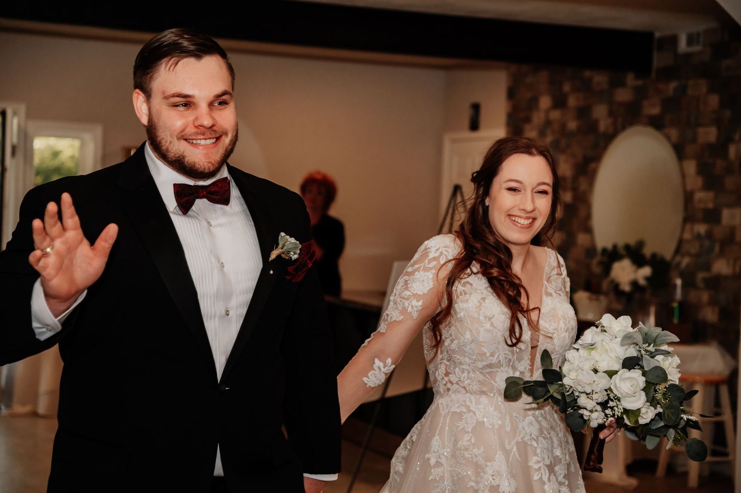 Newlywed couple in wedding attire smiling and waving as they make their grand entrance at their reception.