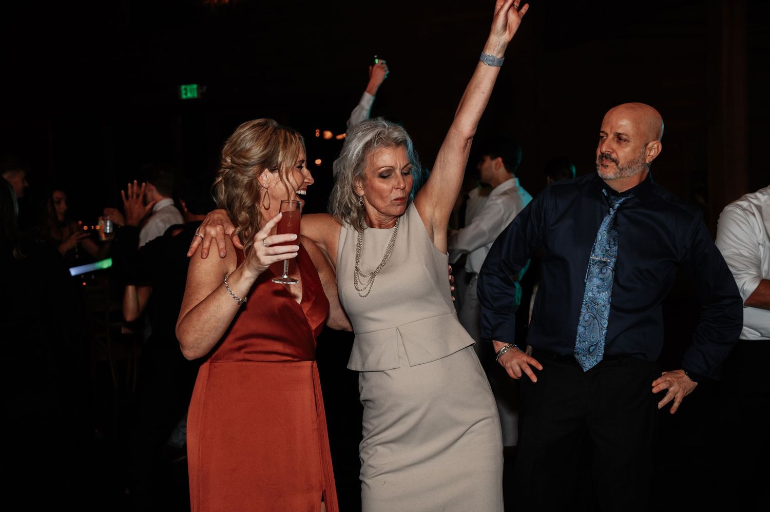 Guests dancing joyfully at wedding reception in dimly lit venue.
