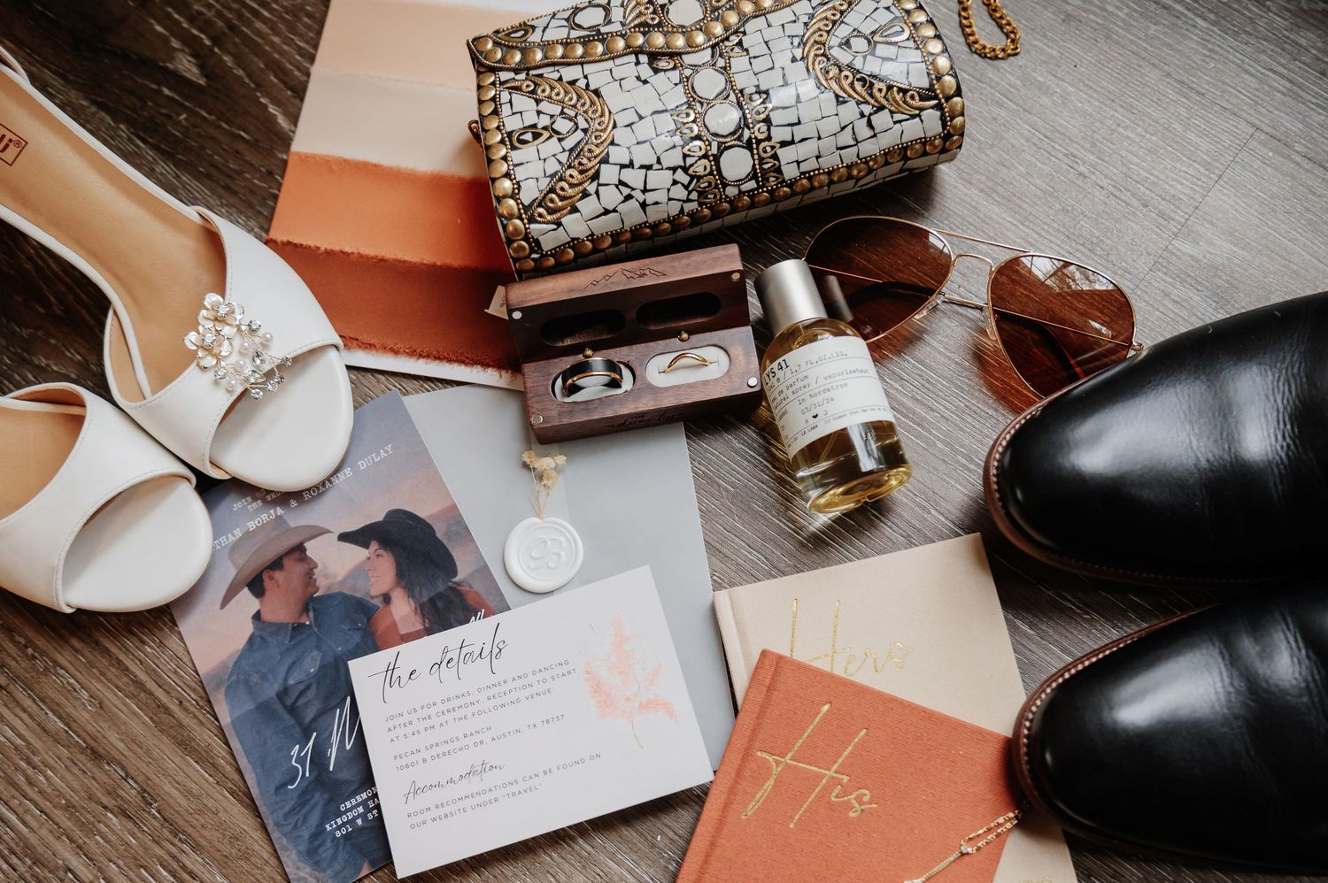 Wedding flat lay with bridal heels, groom shoes, rings, perfume, sunglasses, clutch purse, and elegant invitation suite.