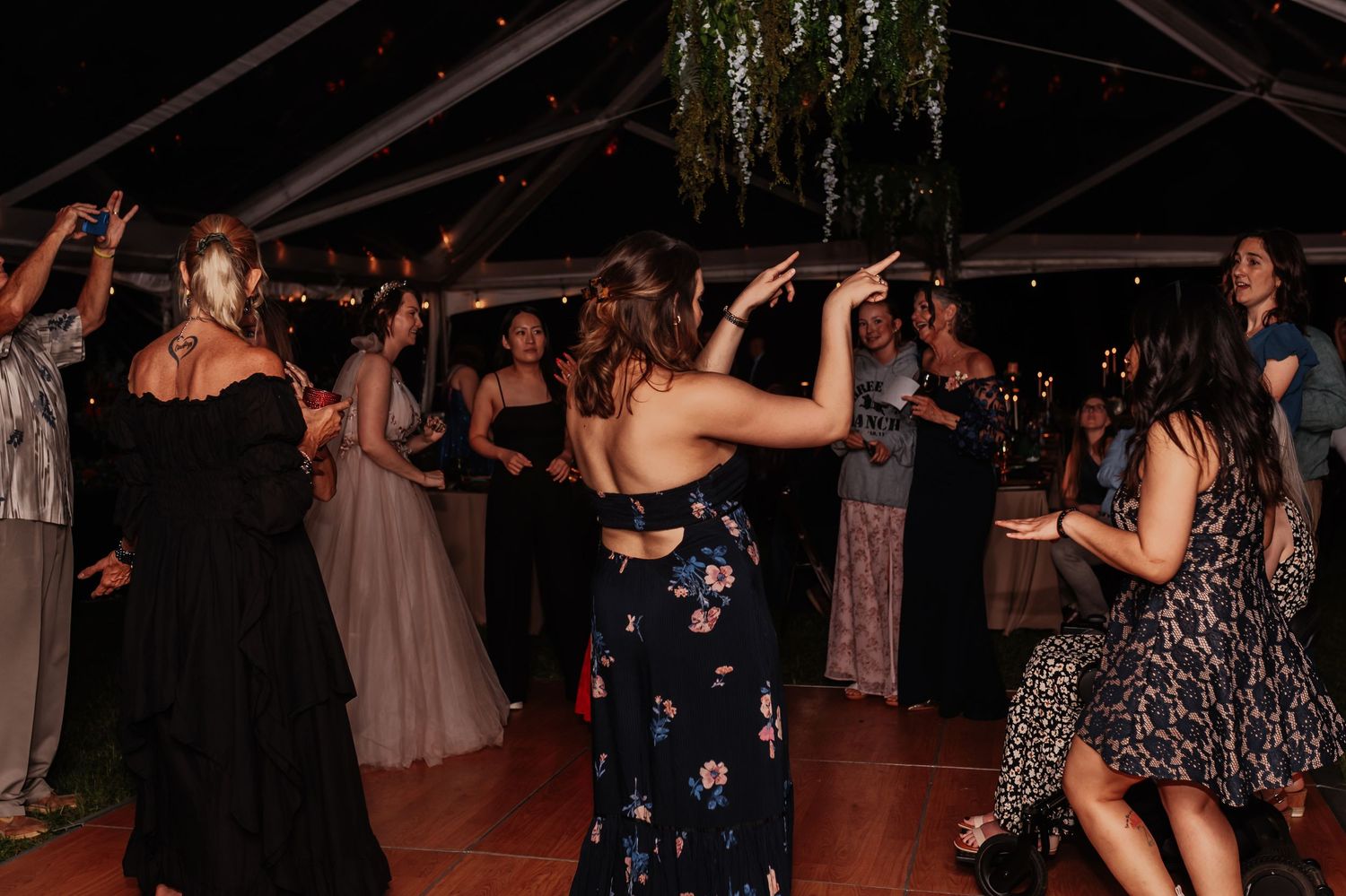Guests dancing joyfully under a clear tent at a lively outdoor wedding reception at night.