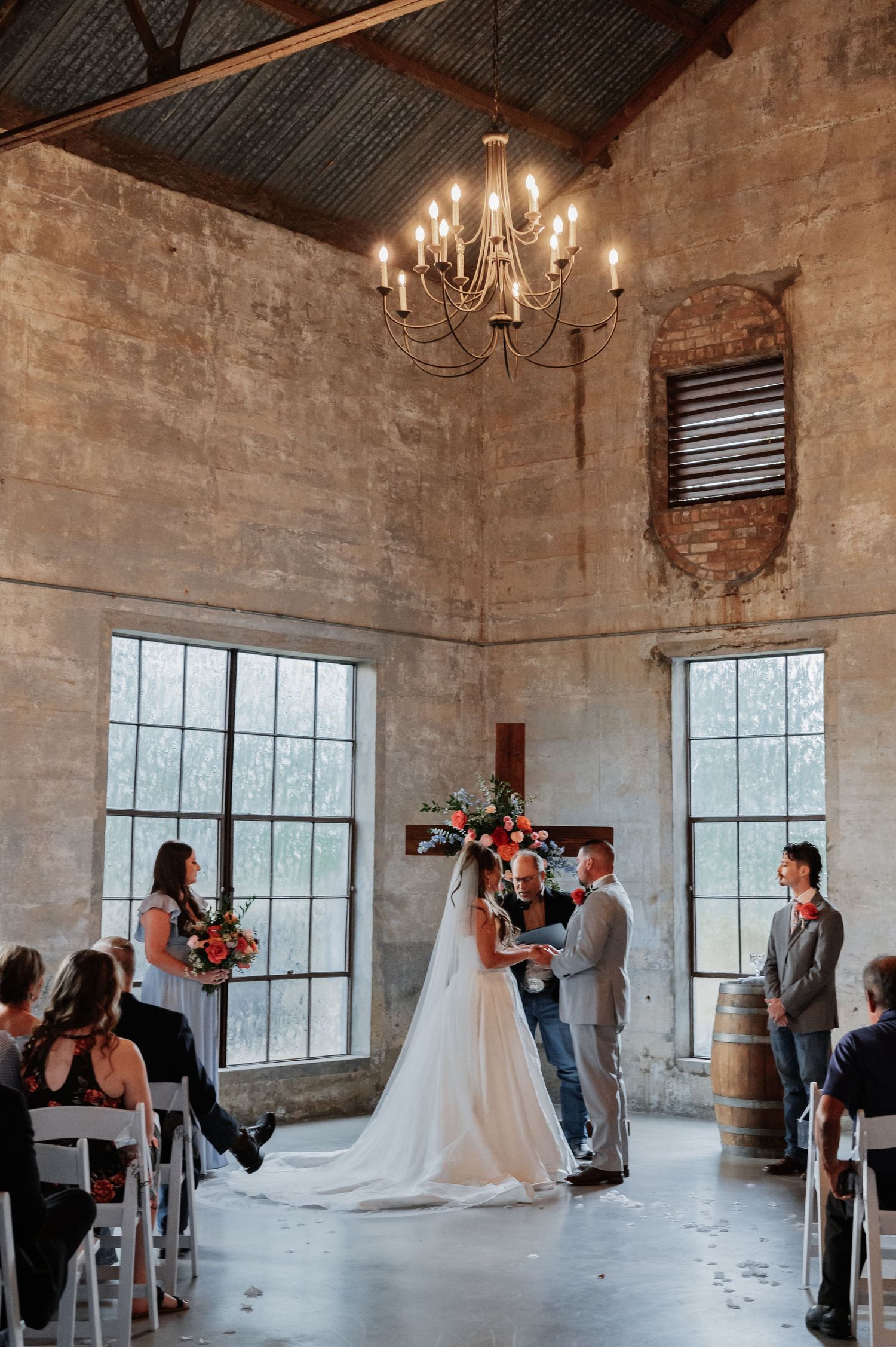 Couple exchanges vows in rustic barn wedding chapel with chandelier and exposed brick walls.