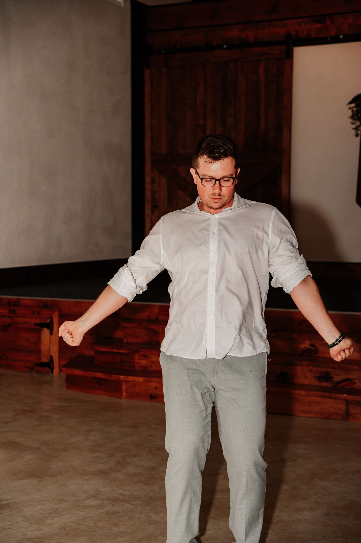 Man in white shirt and gray pants dancing indoors near rustic wooden decor.