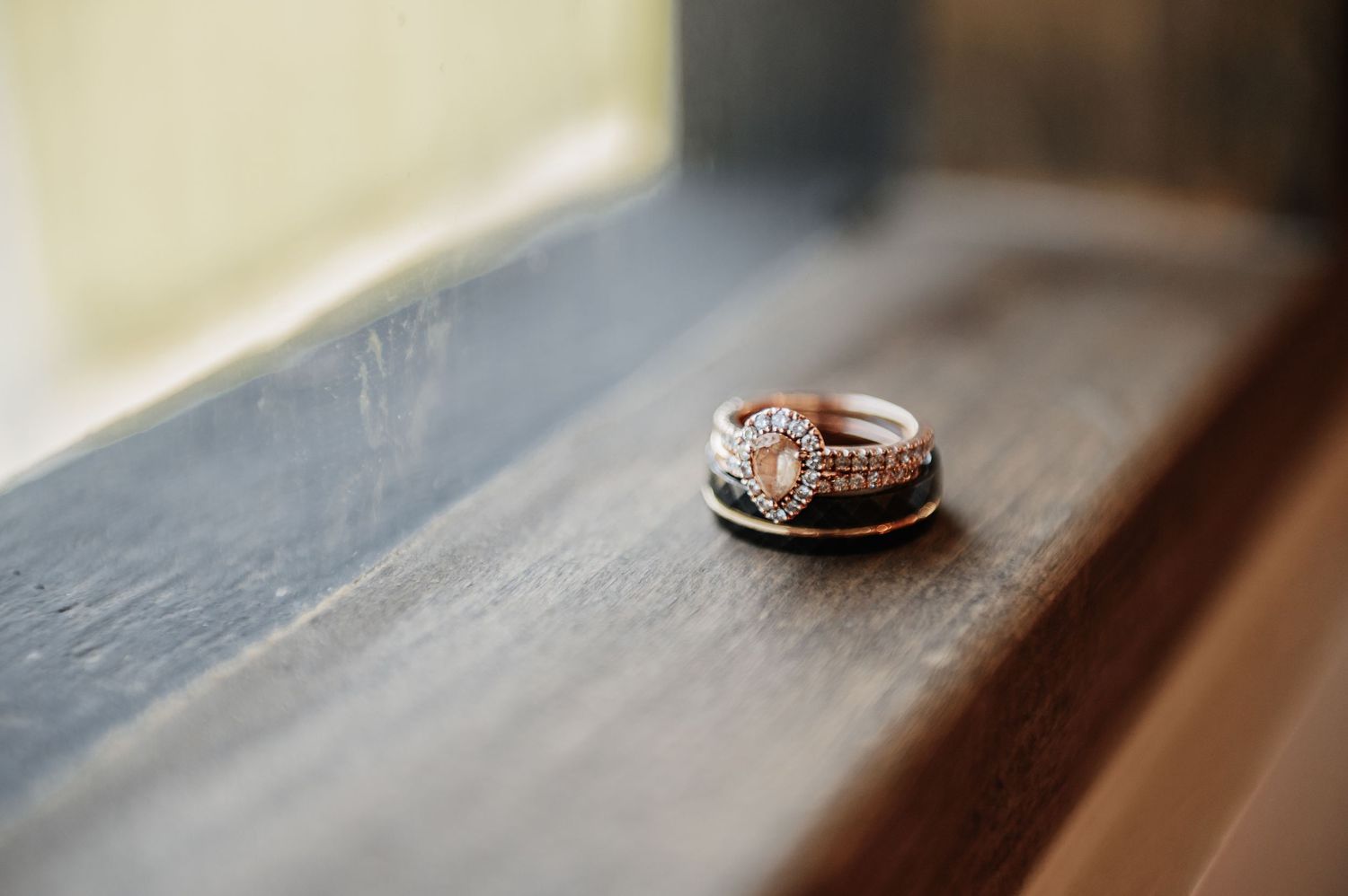 Rose gold engagement ring and wedding band set displayed on a rustic wooden window sill in soft natural light.