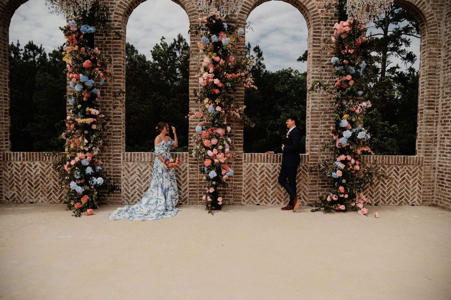 Couple exchanges vows under floral-adorned brick arches with colorful blooms at an elegant outdoor wedding ceremony.