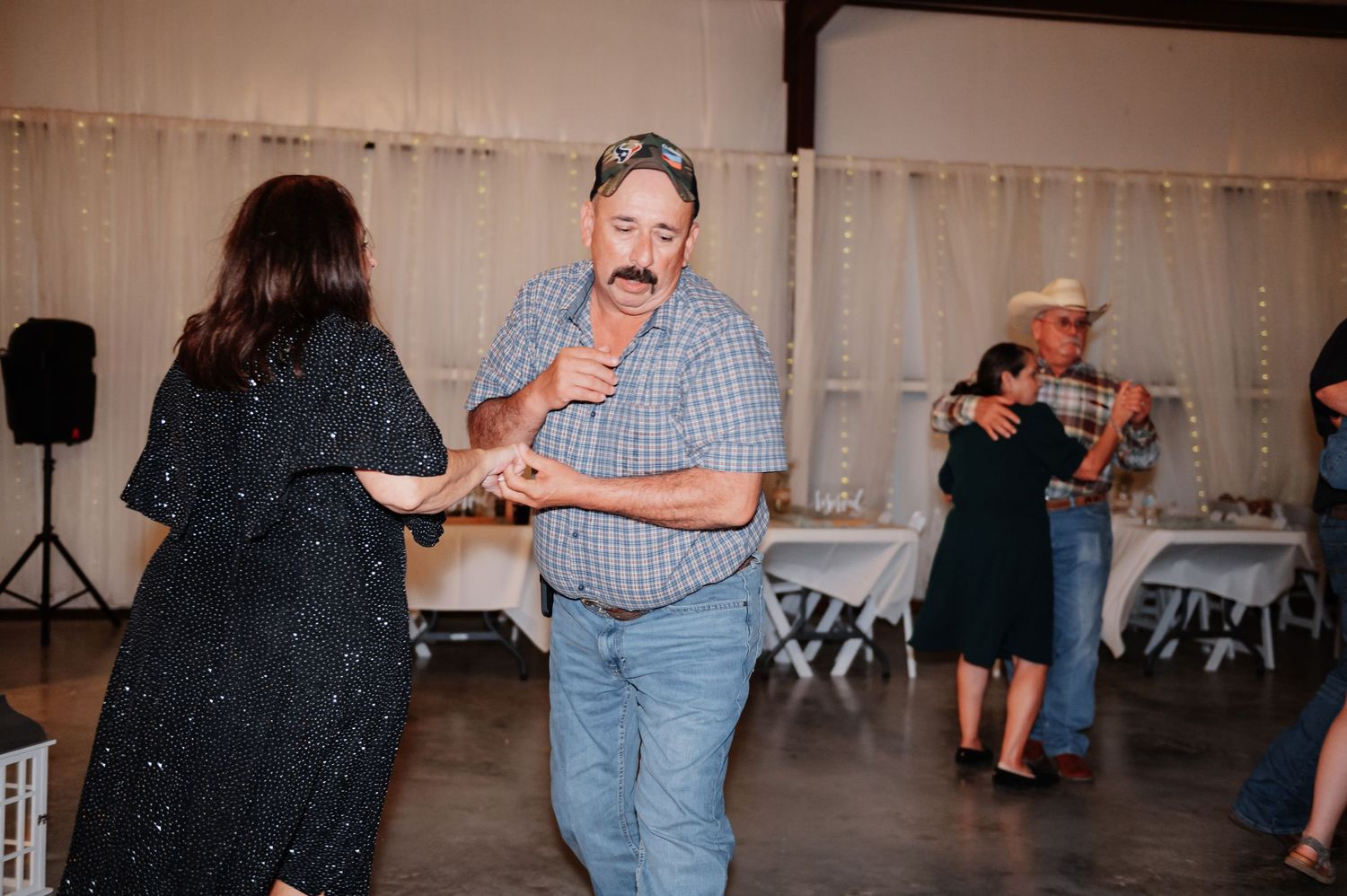 Couple dancing at a country wedding reception in a decorated barn venue with string lights.