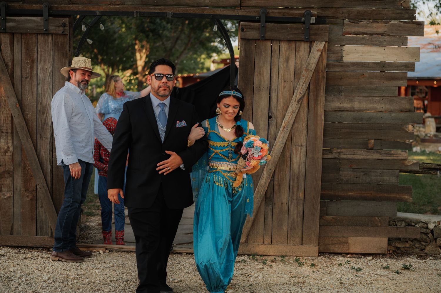 Bride in turquoise dress and groom in black suit walking through barn doors at rustic wedding.