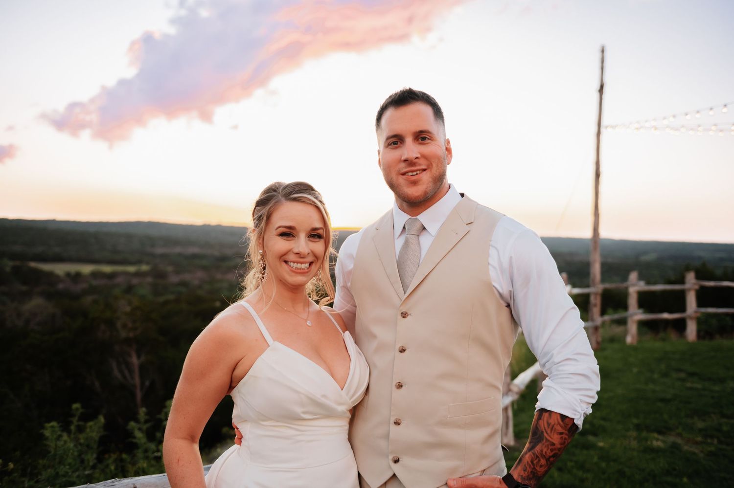 A bride and groom smile together at sunset overlooking a scenic landscape at their outdoor wedding ceremony.