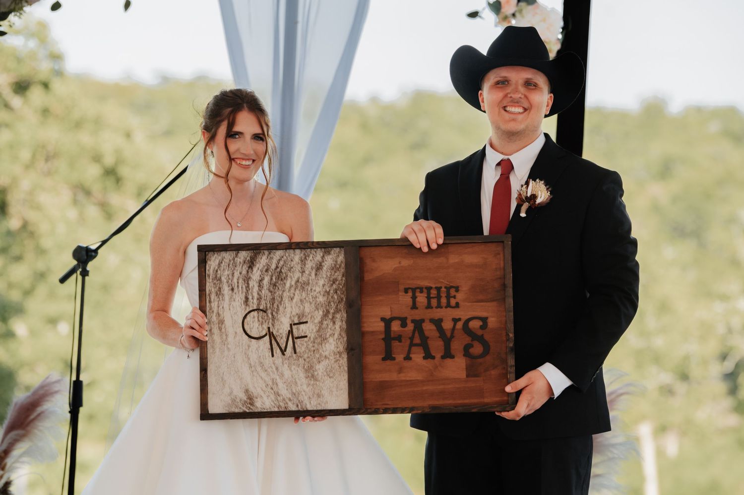Newlyweds hold personalized wooden signs displaying their monogram and The Fays surname at their wedding.
