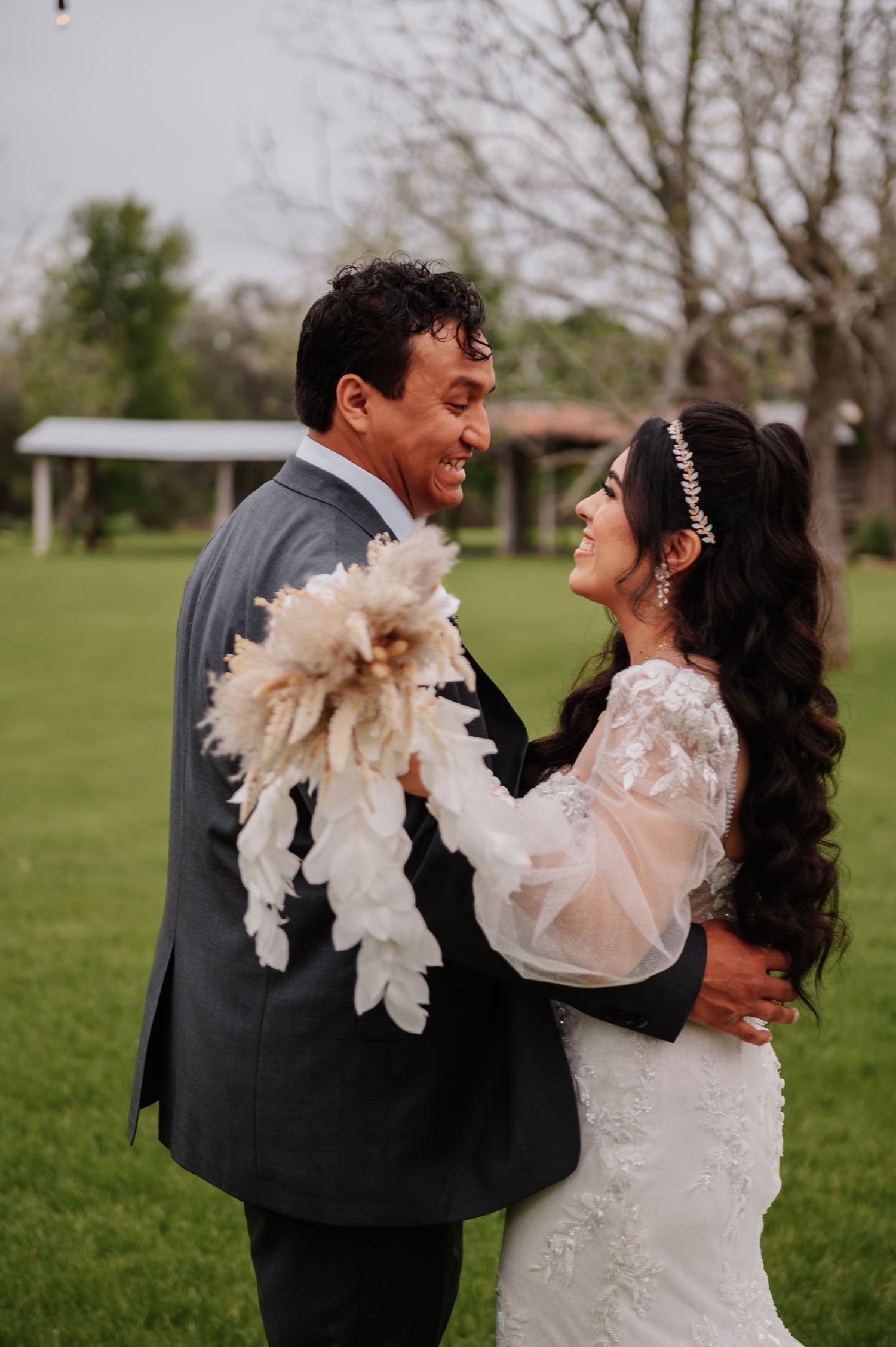 A joyful bride and groom share a romantic moment outdoors, with the bride holding a white feather bouquet.