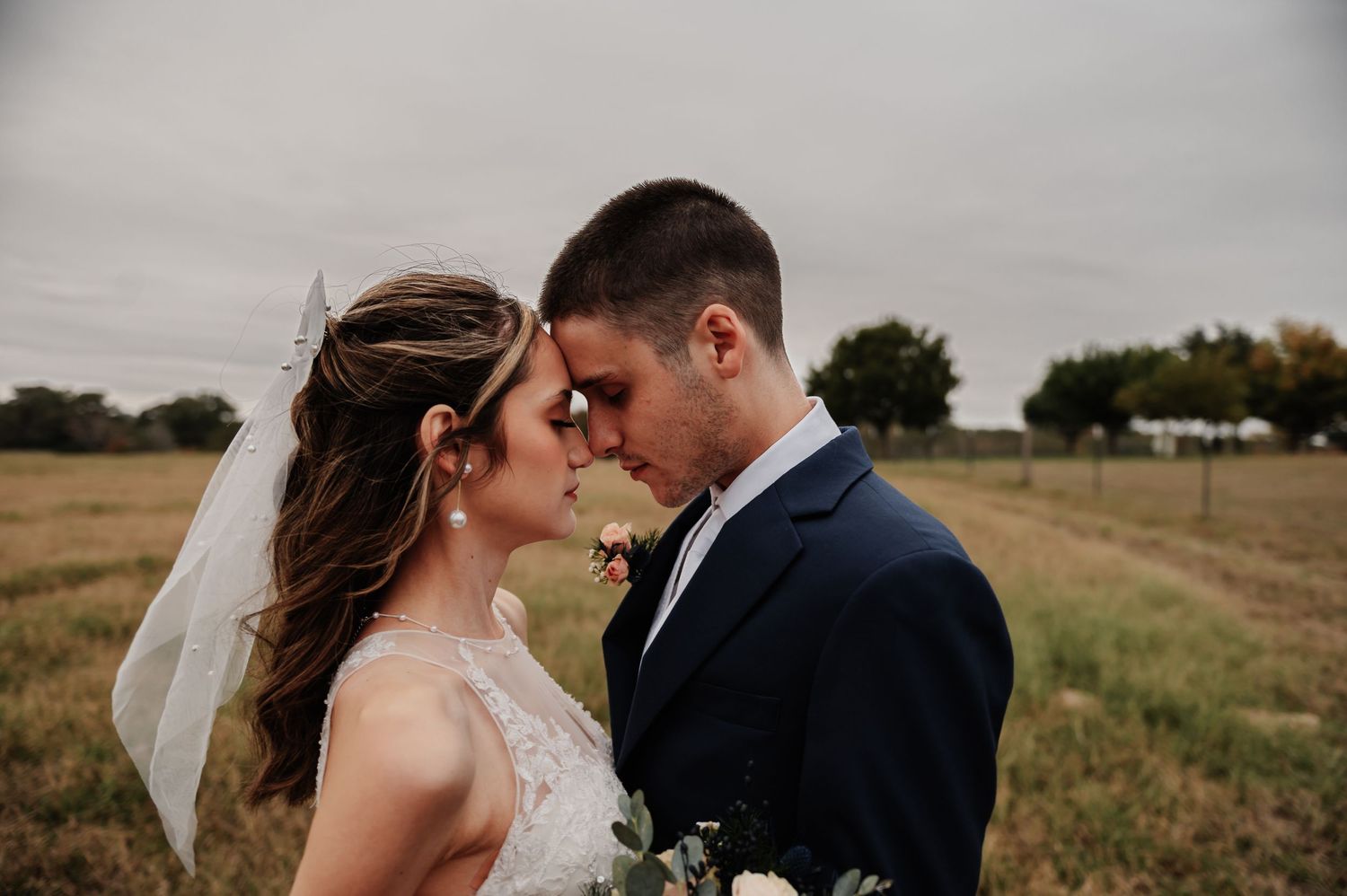 Bride and groom sharing an intimate forehead touch moment outdoors in a rustic field on their wedding day.