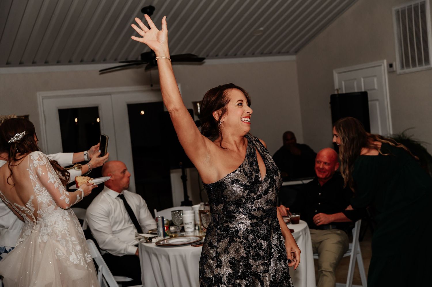 Woman in floral dress dancing joyfully at a wedding reception, raising her arm with a smile.