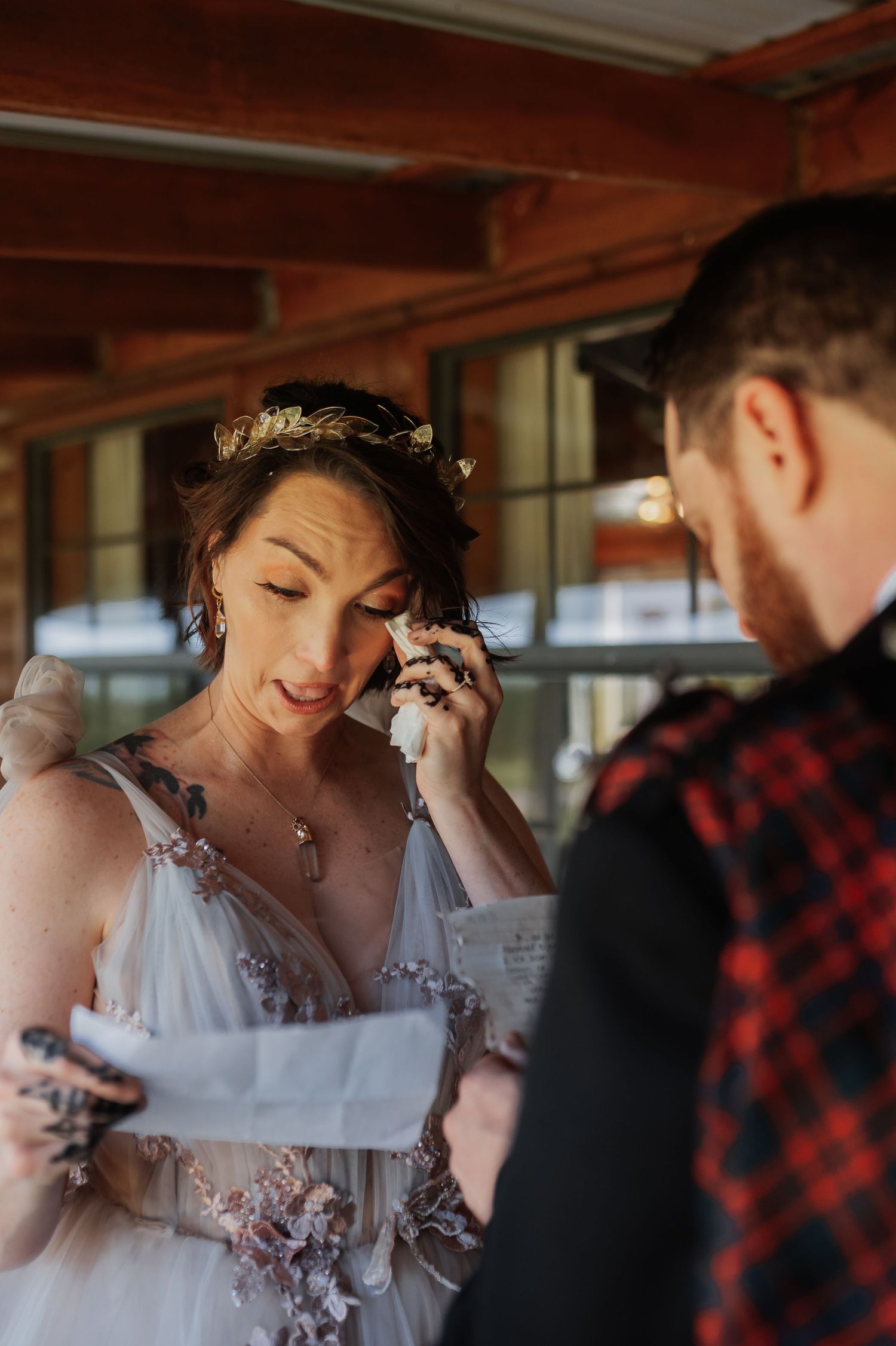 Emotional bride in floral crown wiping tears while reading wedding vows, wearing a delicate tulle gown.