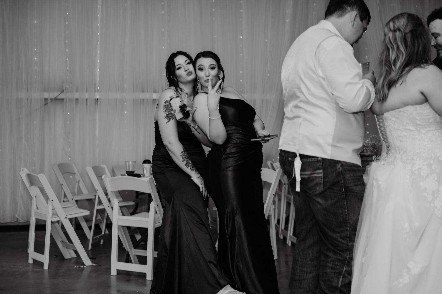 Two women in black dresses pose together on a wedding reception dance floor in black and white photo.