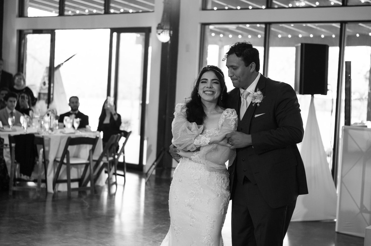 Black and white photo of a bride and groom sharing their first dance at a wedding reception.