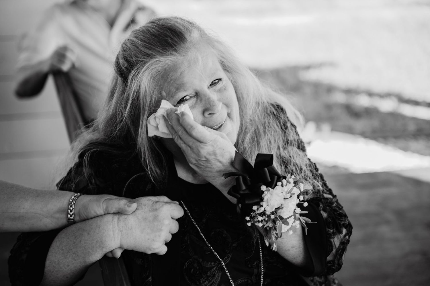 Emotional woman wiping tears at a wedding, wearing a floral corsage, in black and white photography.