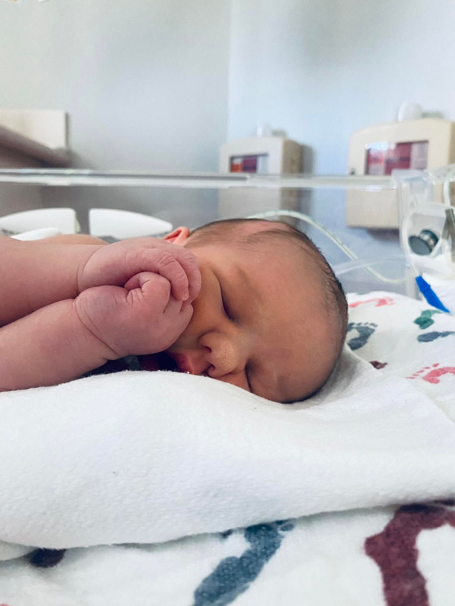 Newborn baby sleeping peacefully in hospital nursery on white blanket, tiny fists curled near face.
