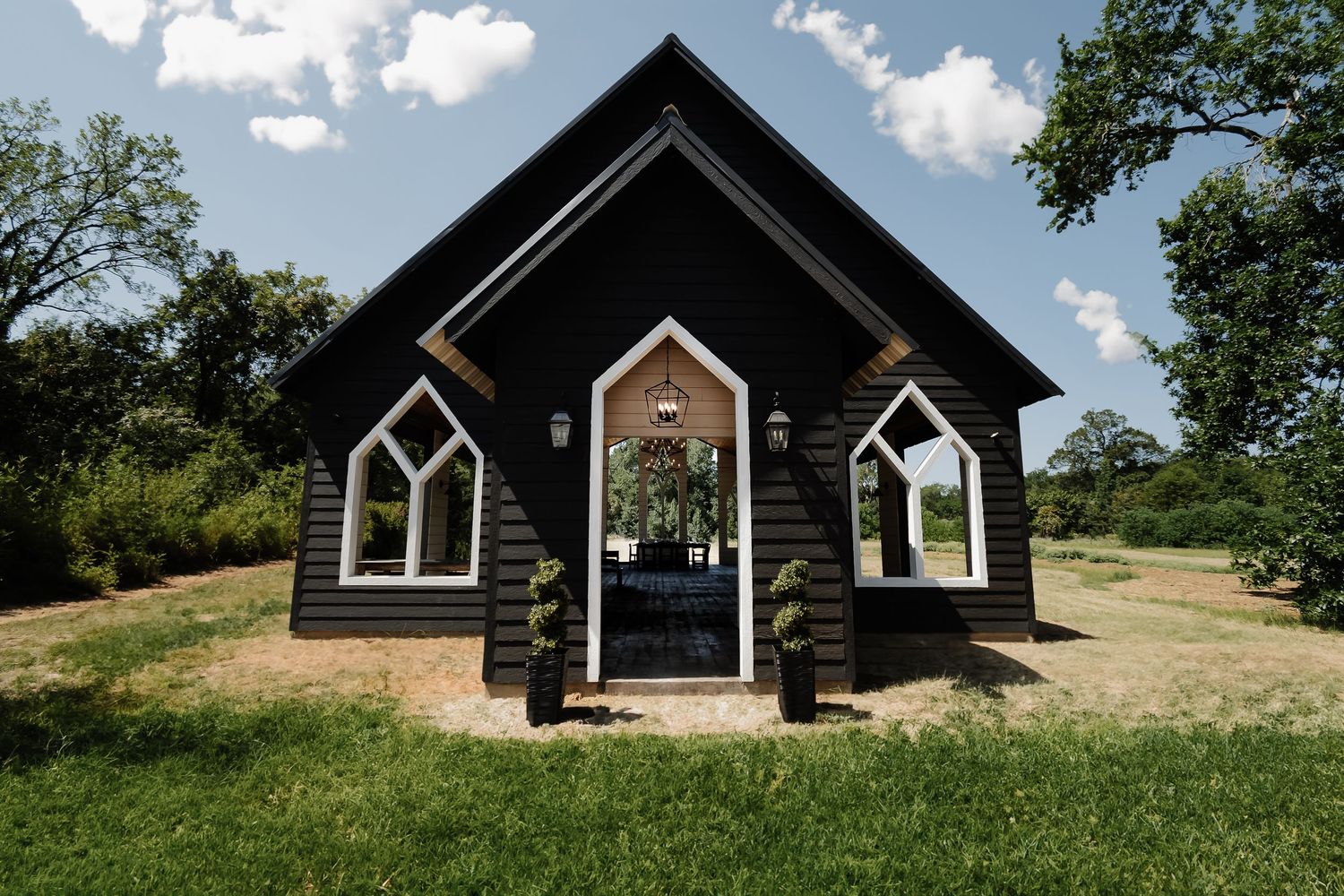 A charming black Gothic-style chapel with arched windows and topiary shrubs, set in a lush green landscape.