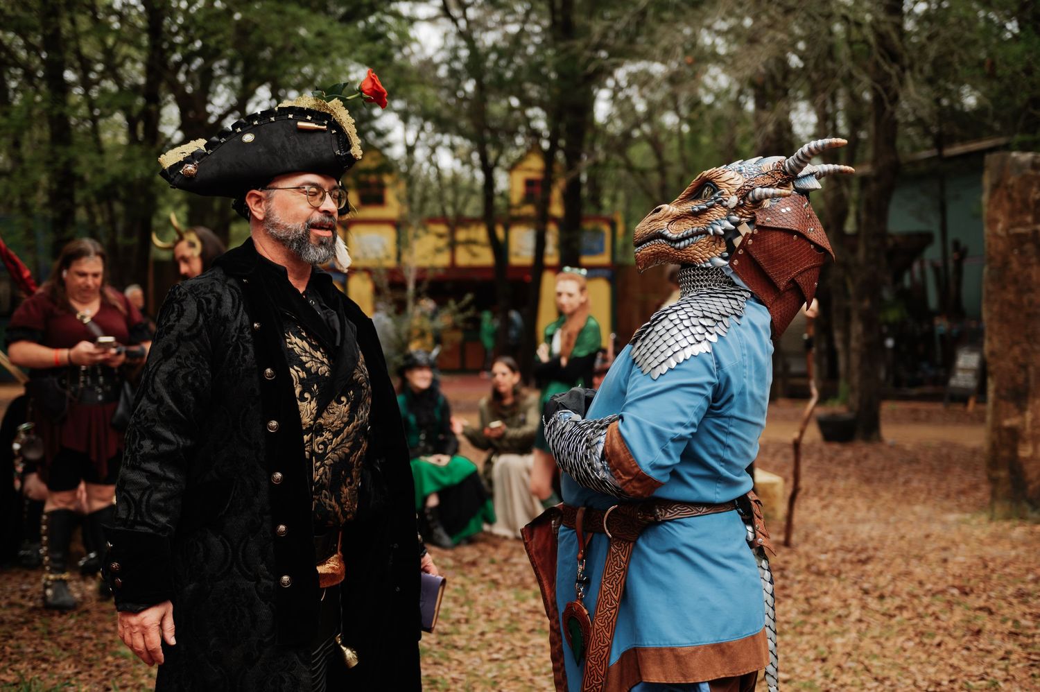 Two men in Renaissance faire costumes, one in pirate hat and one in blue armor with horned helmet, converse outdoors.